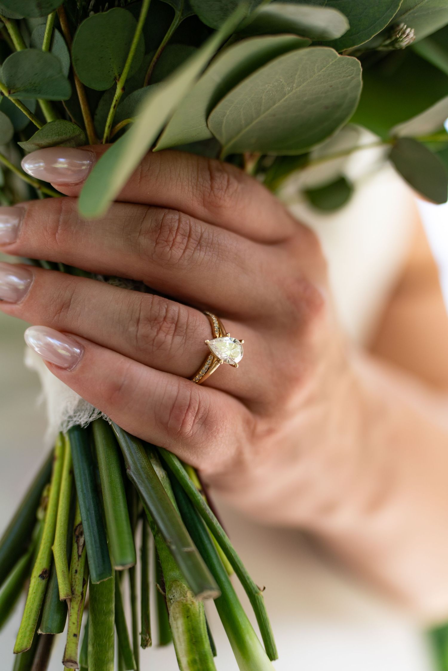 Wedding bouquet with green foliage held by hands wearing elegant engagement ring.