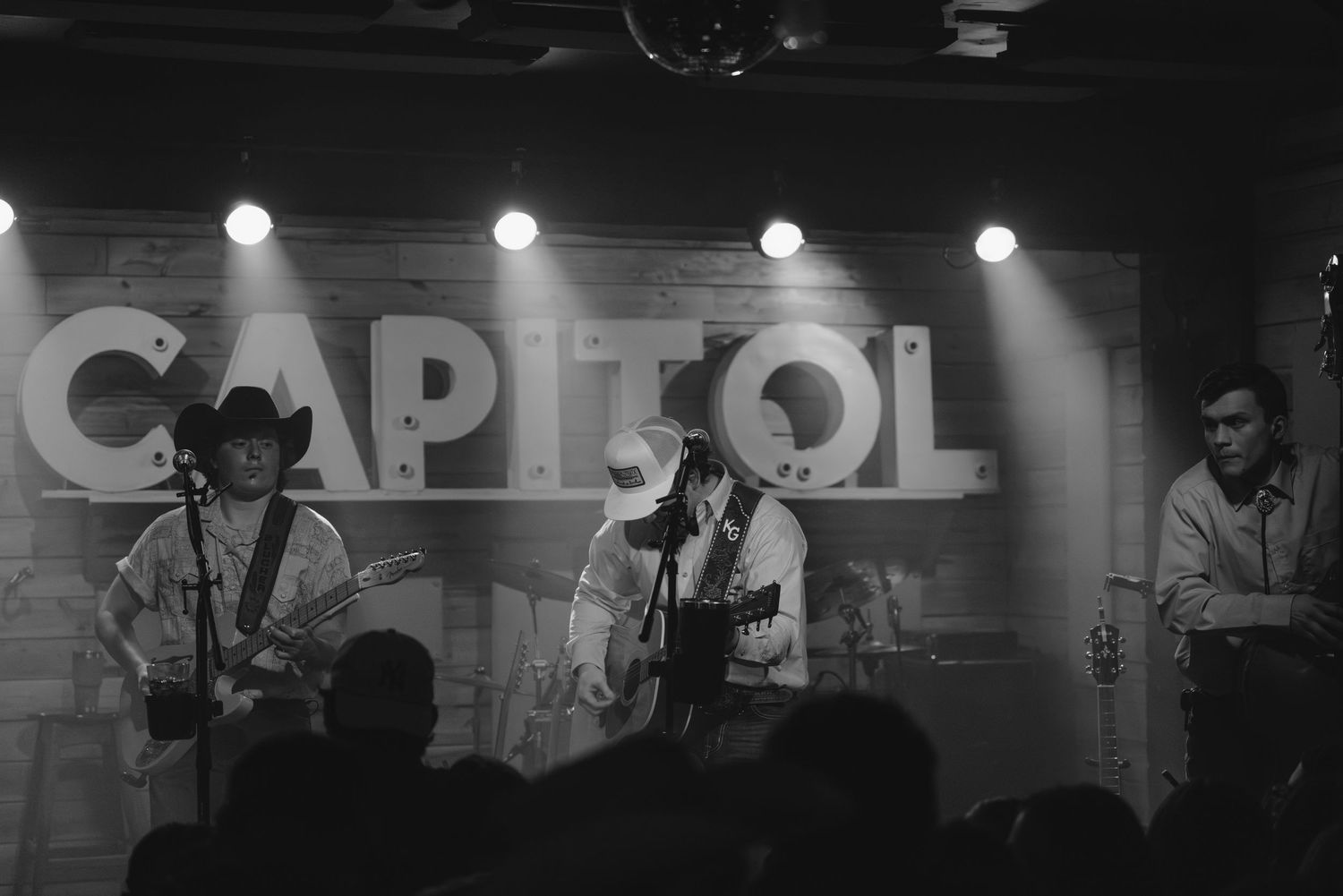 Musicians performing on stage at Capitol venue with dramatic lighting and silhouetted figures.