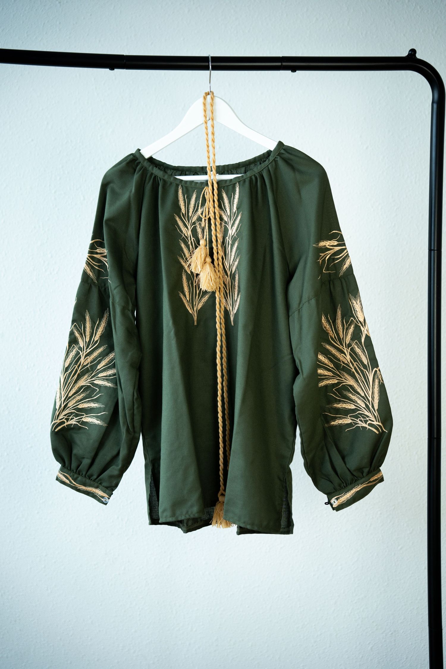 Dark green blouse with golden wheat stalk embroidery on display.