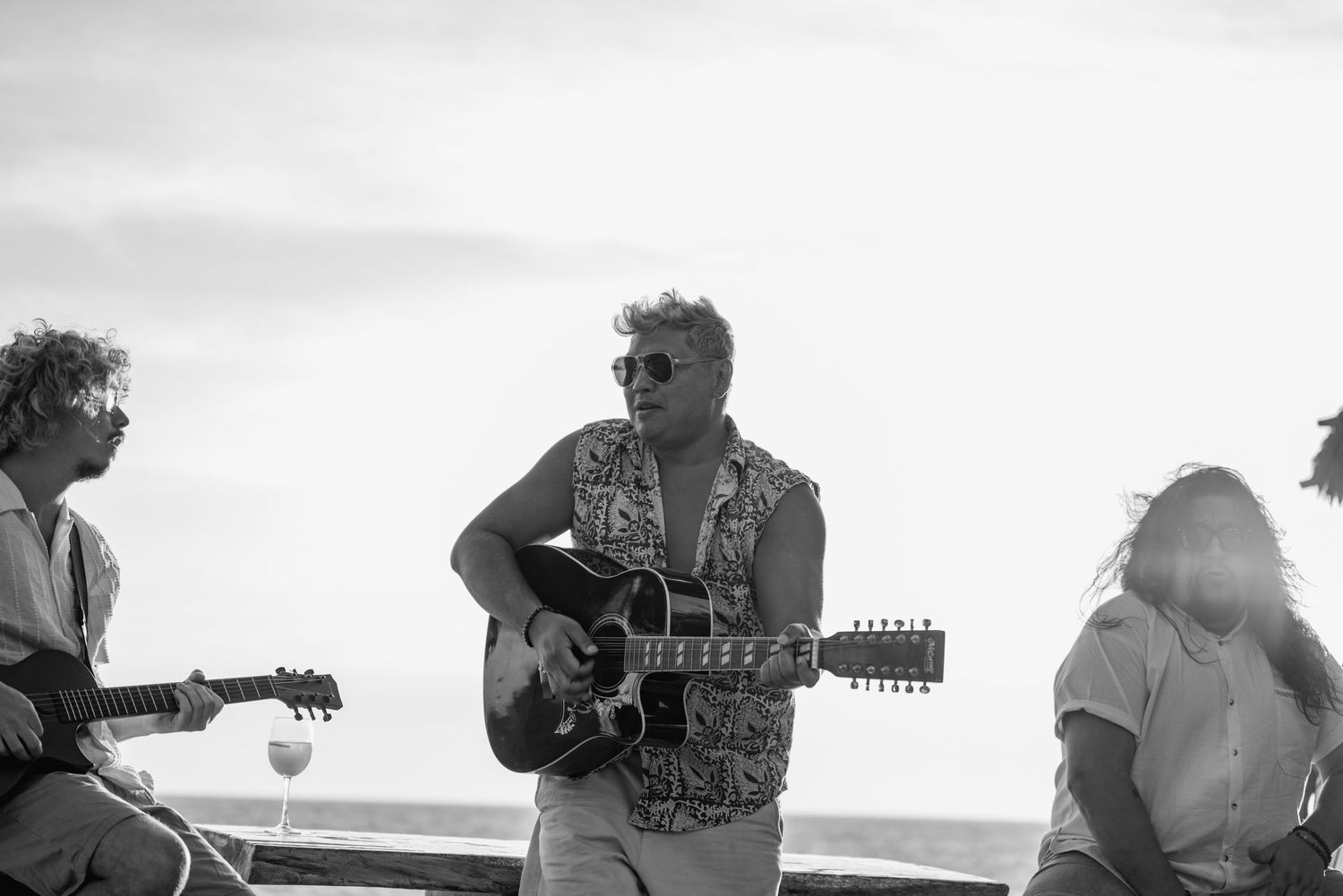 Musicians performing with guitars on a beach at sunset.