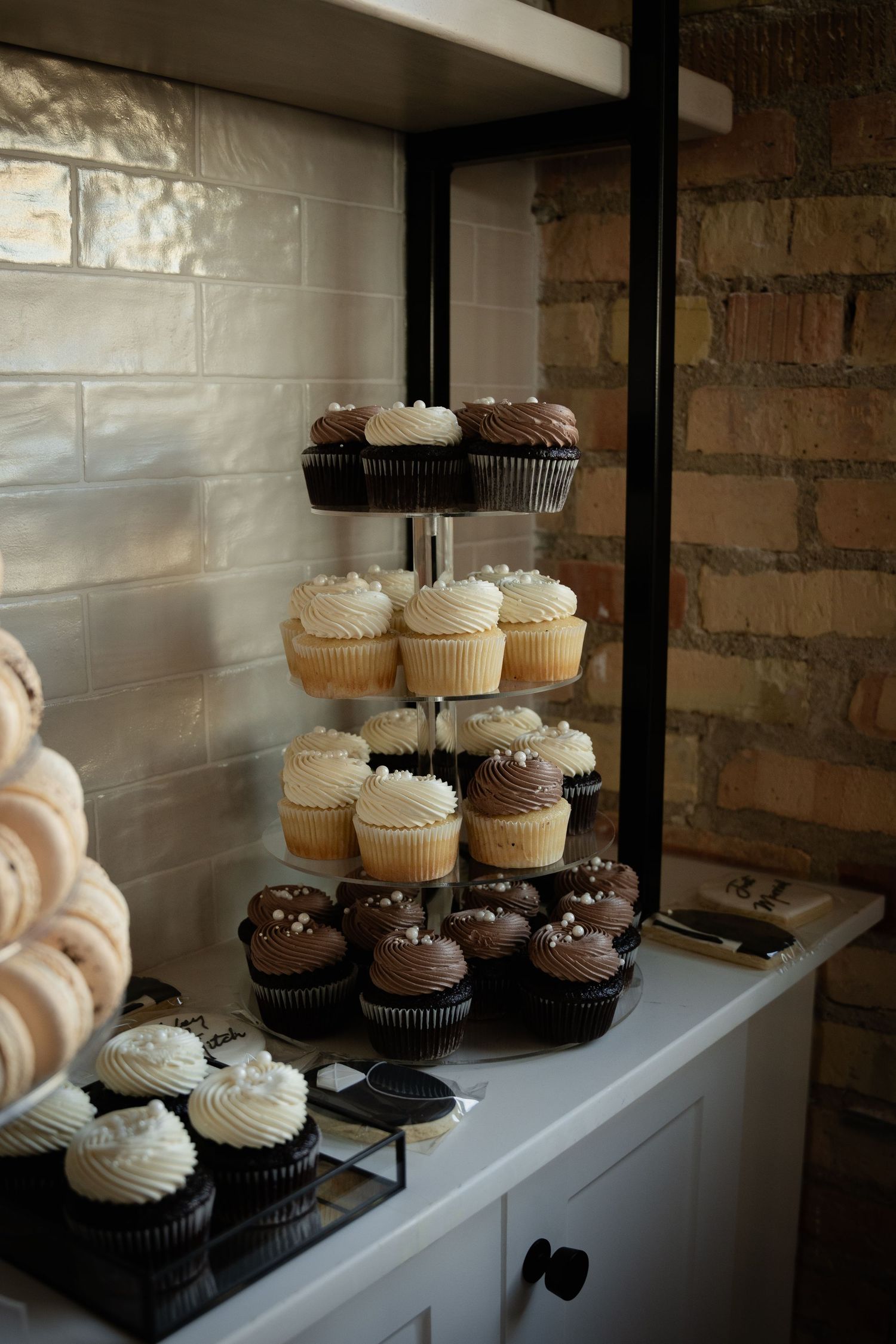 Tiered display of chocolate and vanilla cupcakes with frosting on white cabinet.