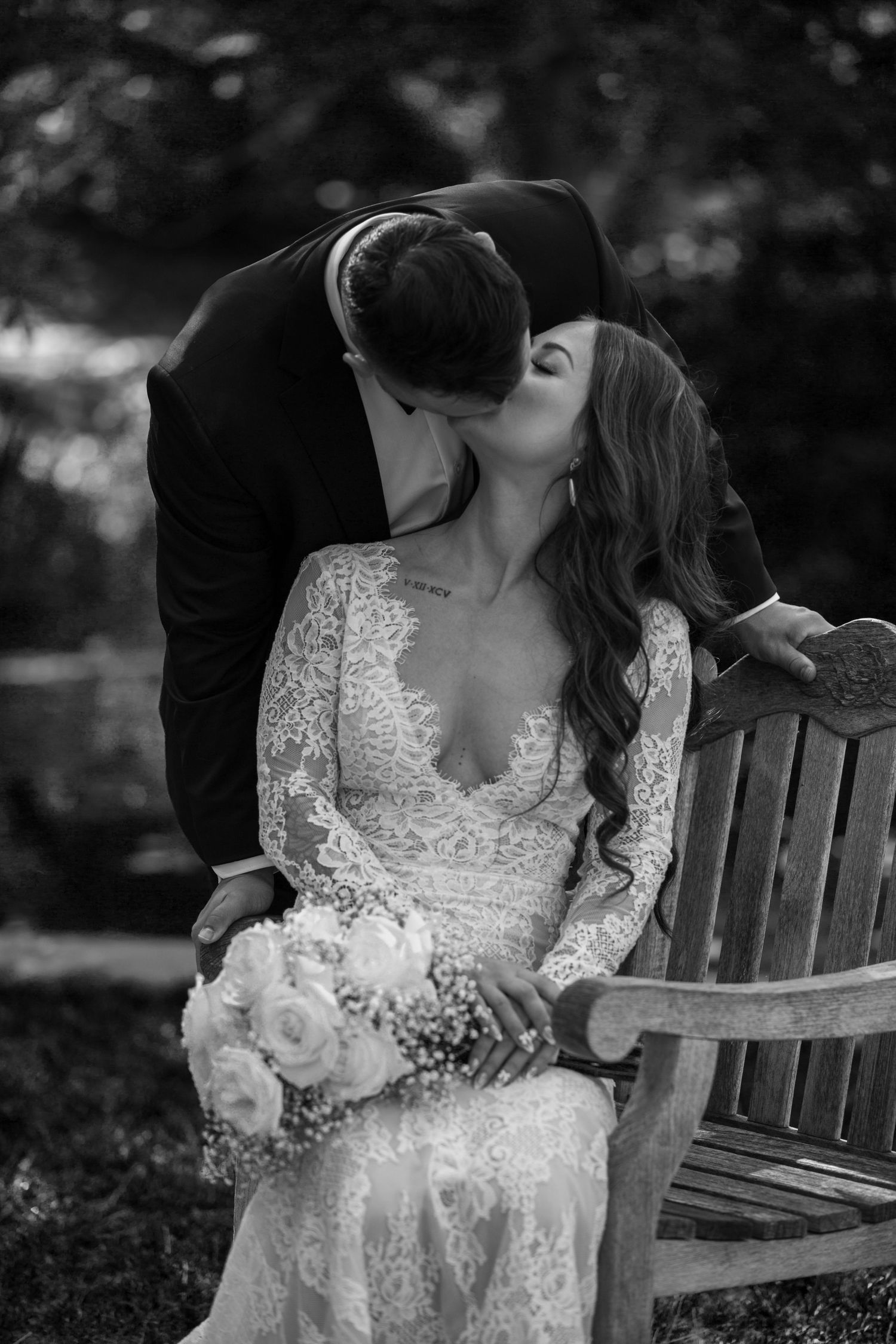 Romantic black and white wedding portrait of couple sharing intimate moment on wooden bench.