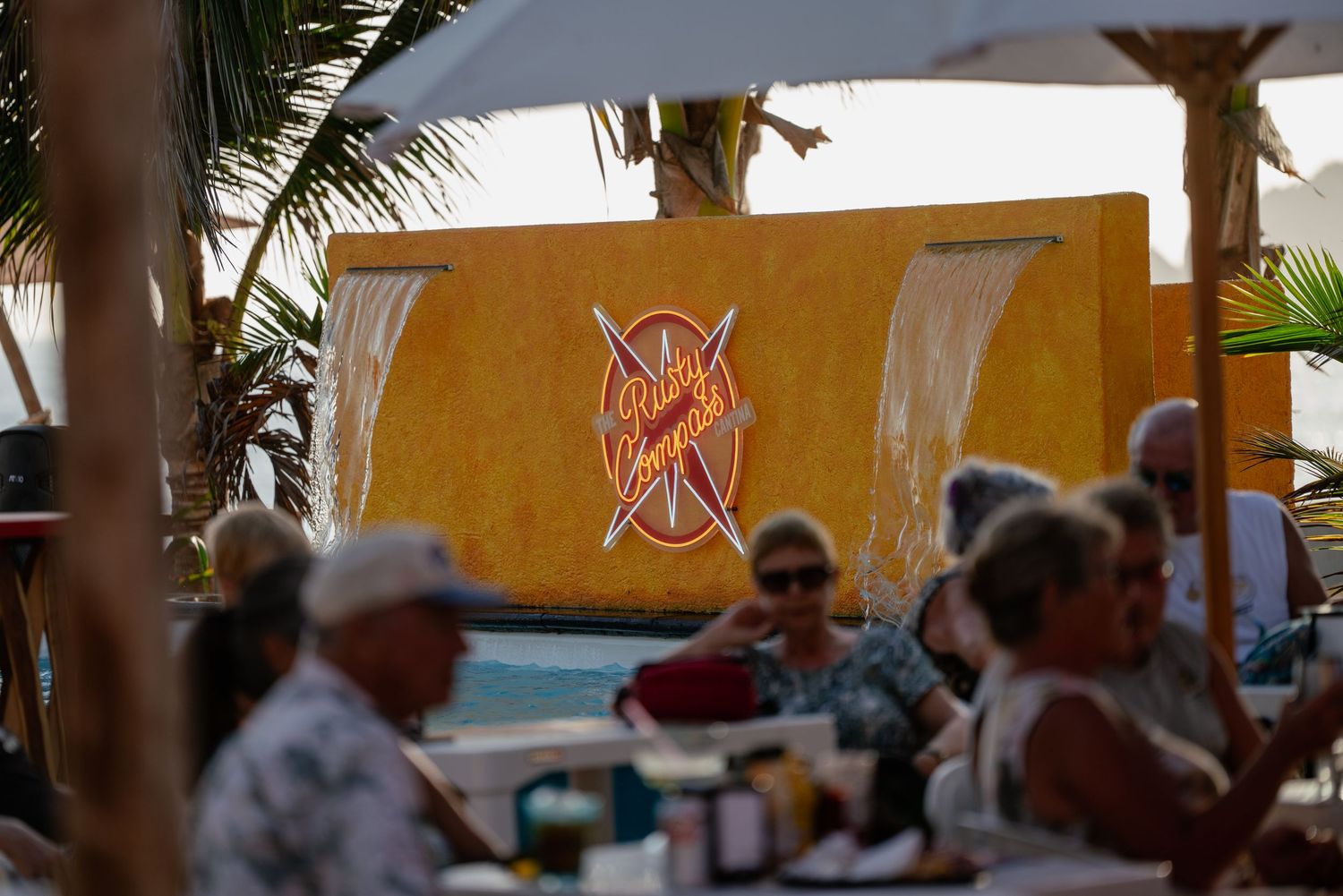 Beachfront restaurant with red umbrellas and palm trees creating a tropical dining atmosphere.
