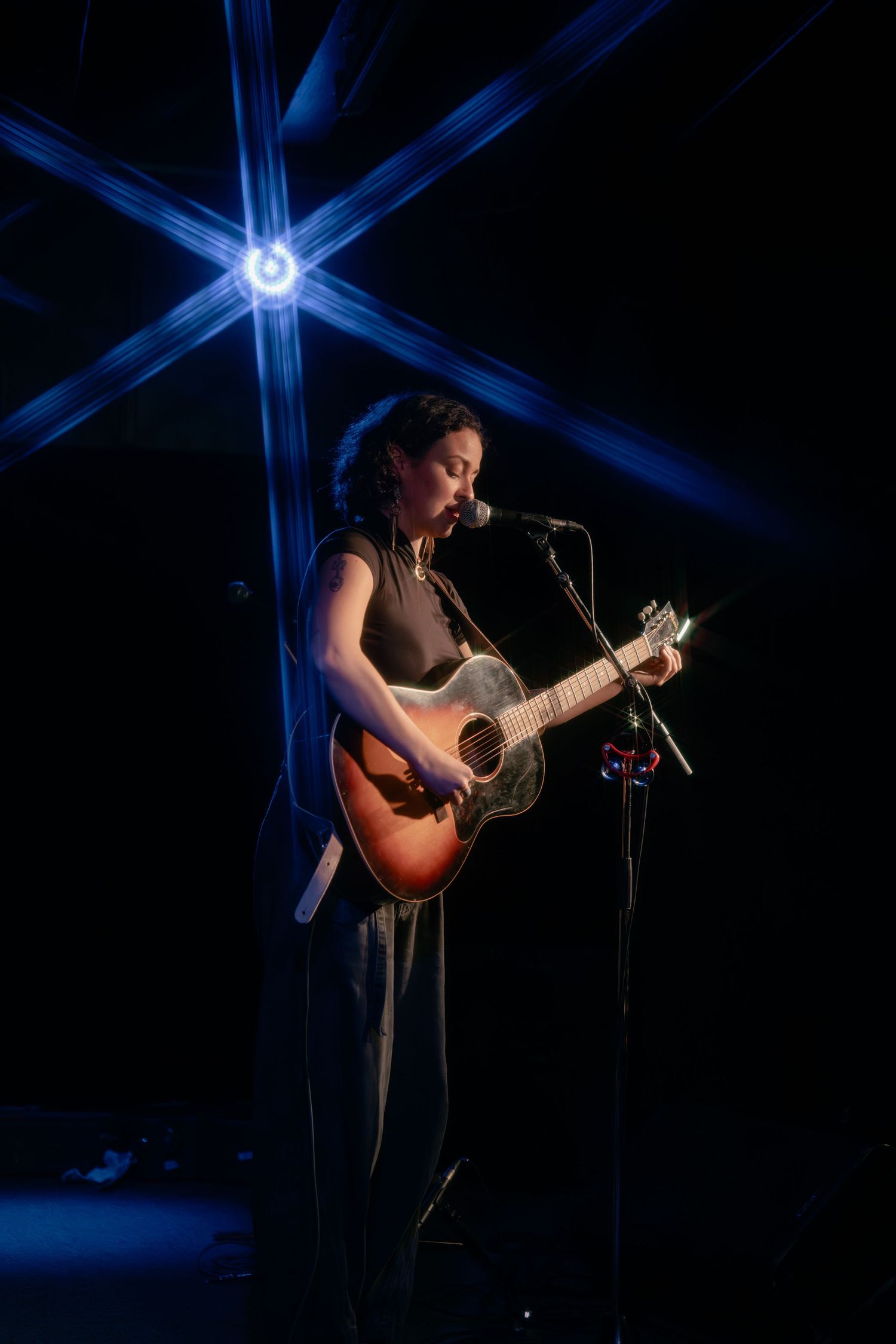 Solo acoustic performance under blue cross-shaped stage lighting.