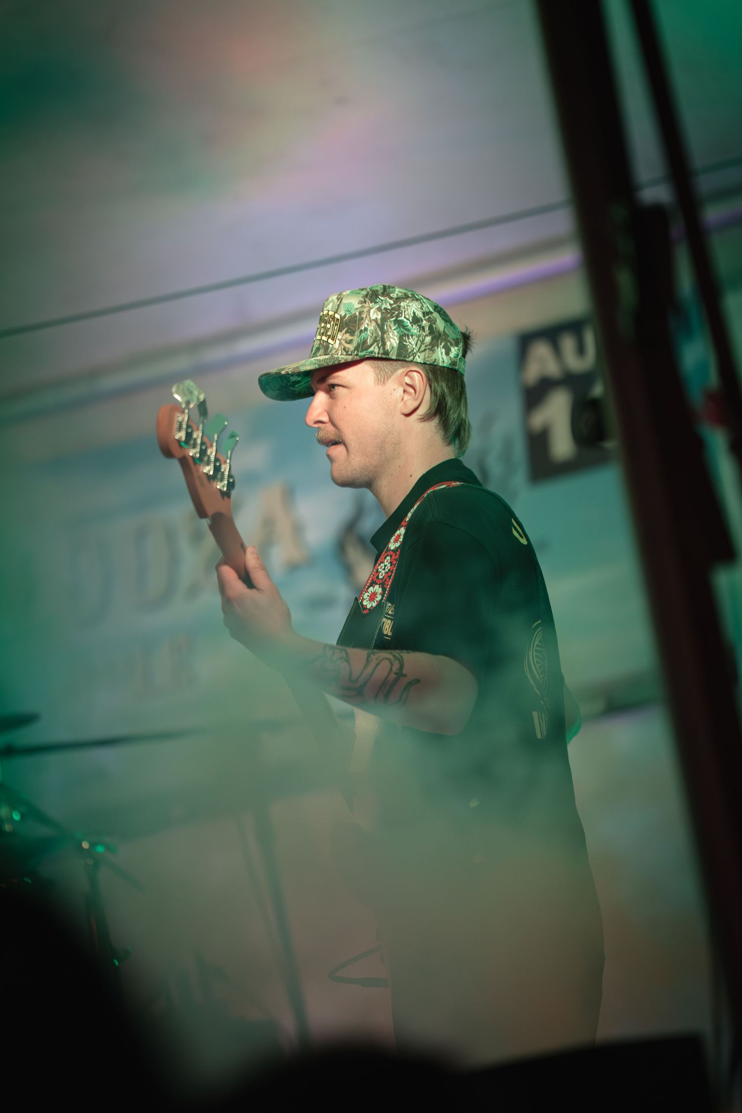 Performer in a baseball cap on stage with green lighting effects.