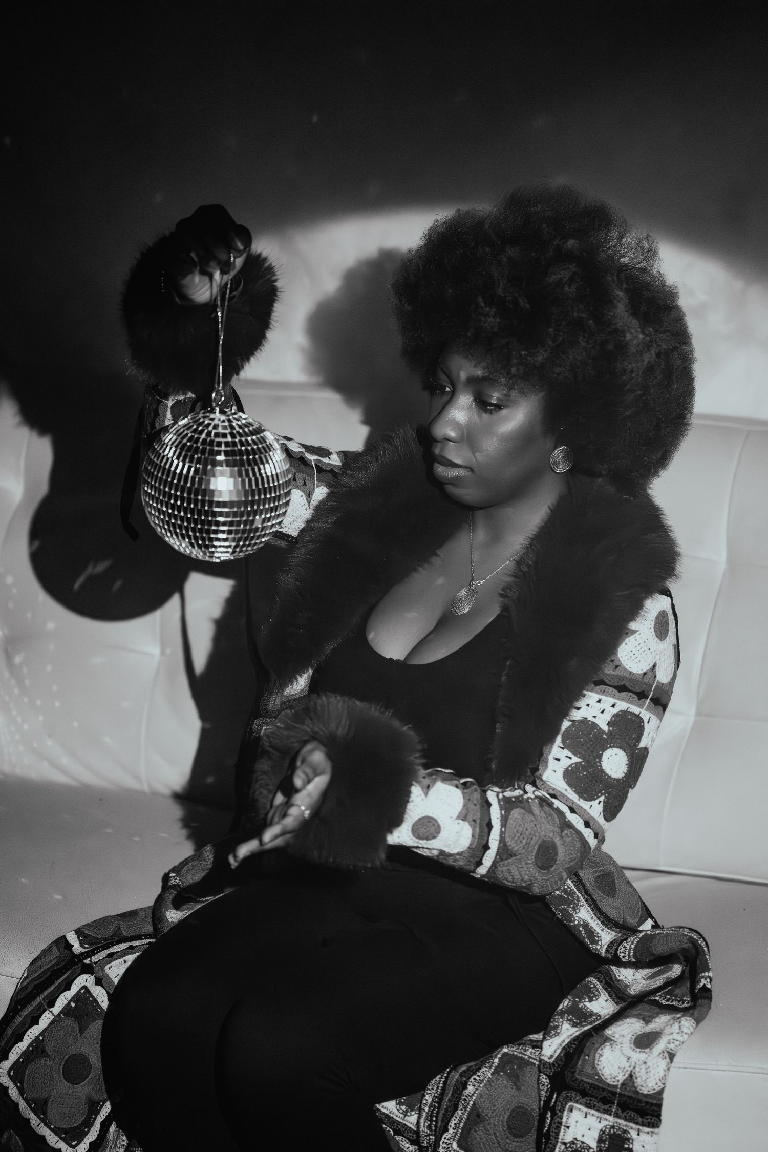 Dramatic black and white portrait with disco ball and floral print outfit on white couch.