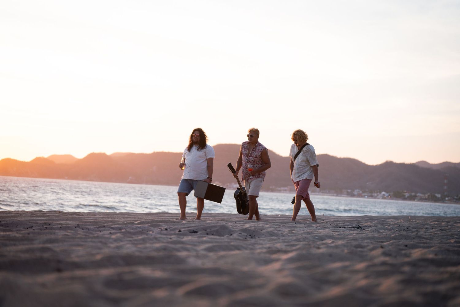 People walking along a beach at sunset with mountains in the background.