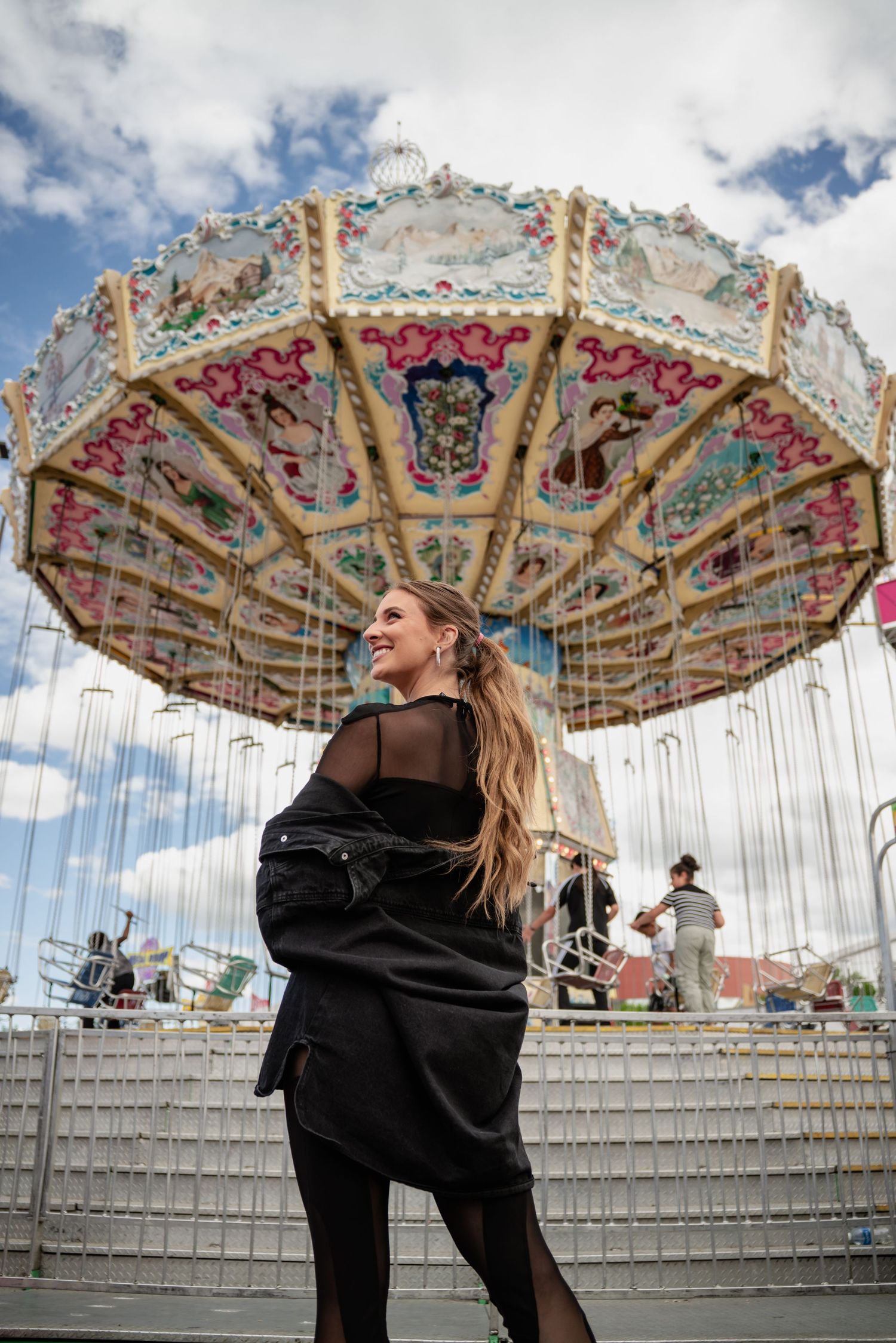 Vintage carousel at an amusement park against blue sky with white clouds.