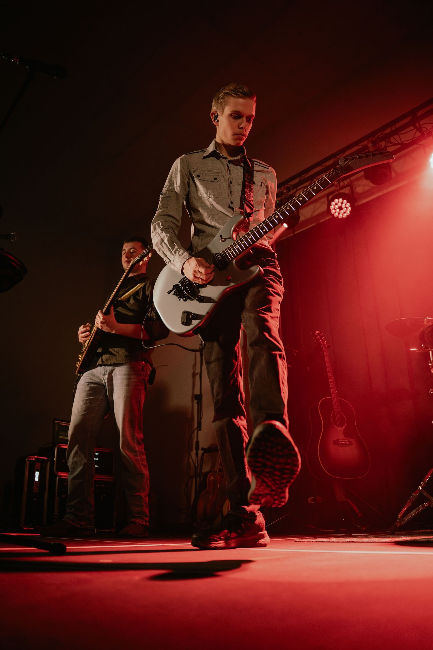 Guitarist performs on red-lit stage in dramatic low angle shot.