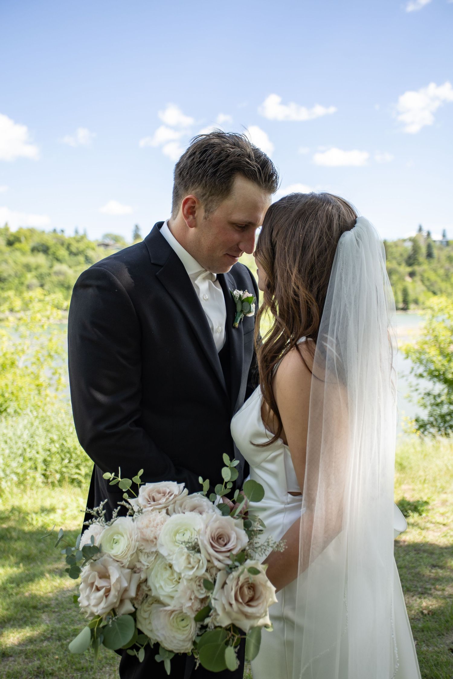 Newlyweds share intimate moment outdoors with bridal bouquet.