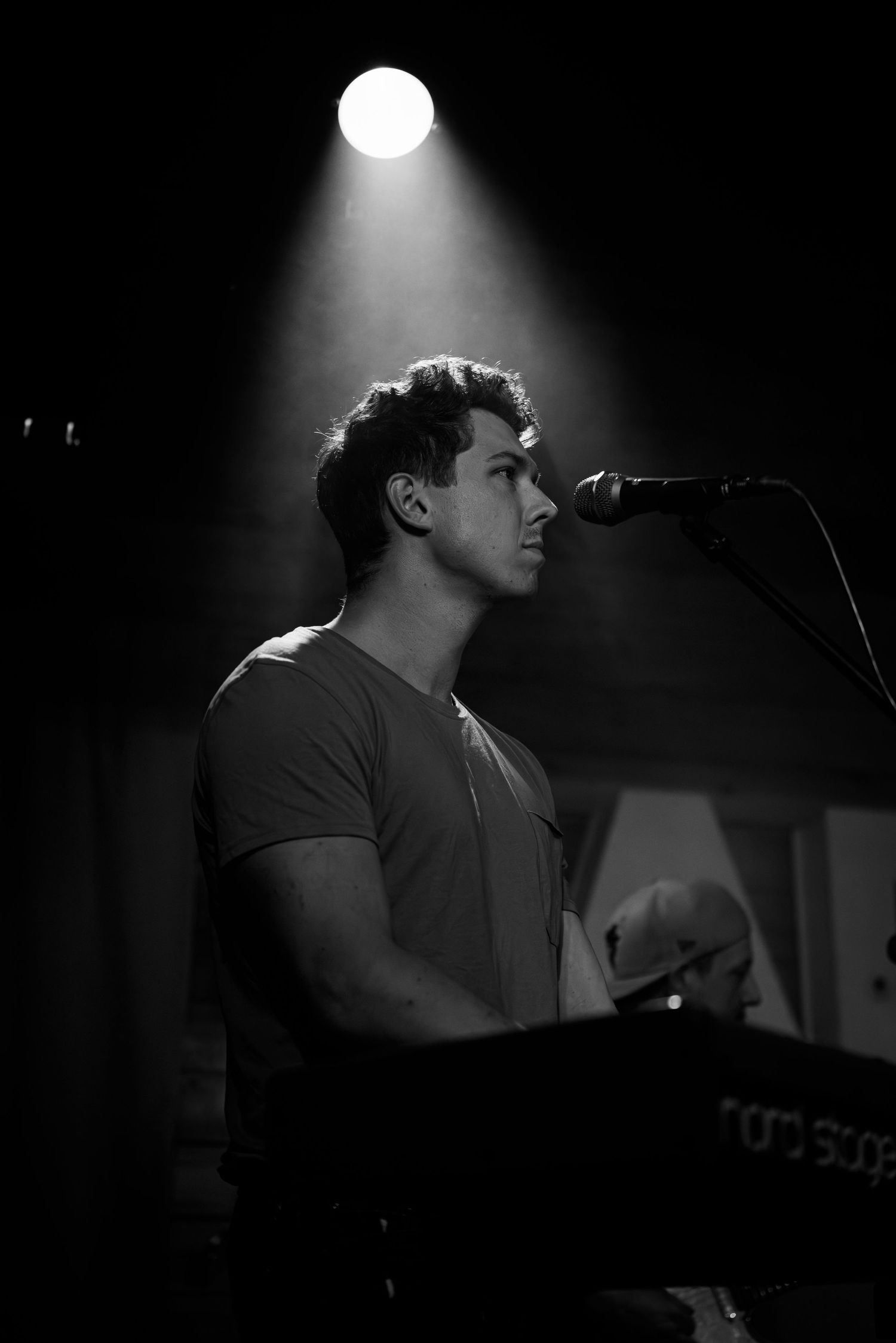 Dramatic spotlight illuminates musician performing at keyboard in dark venue.