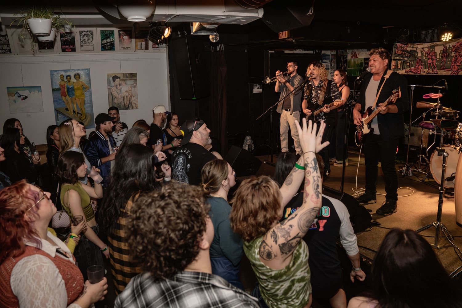 Enthusiastic crowd at music venue with raised hands enjoying live performance.