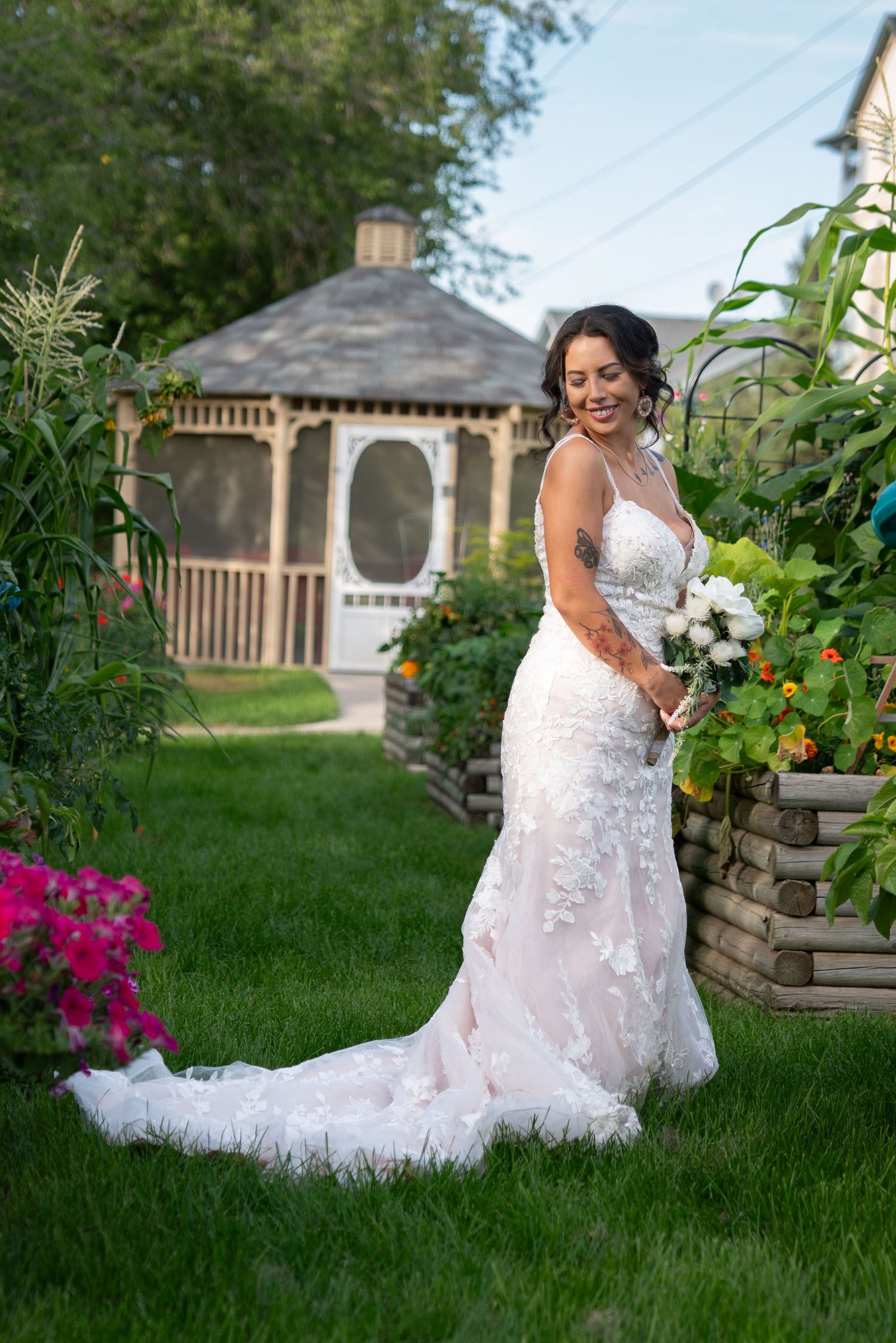 Wedding dress with intricate lace details photographed in a garden setting with blooming flowers.