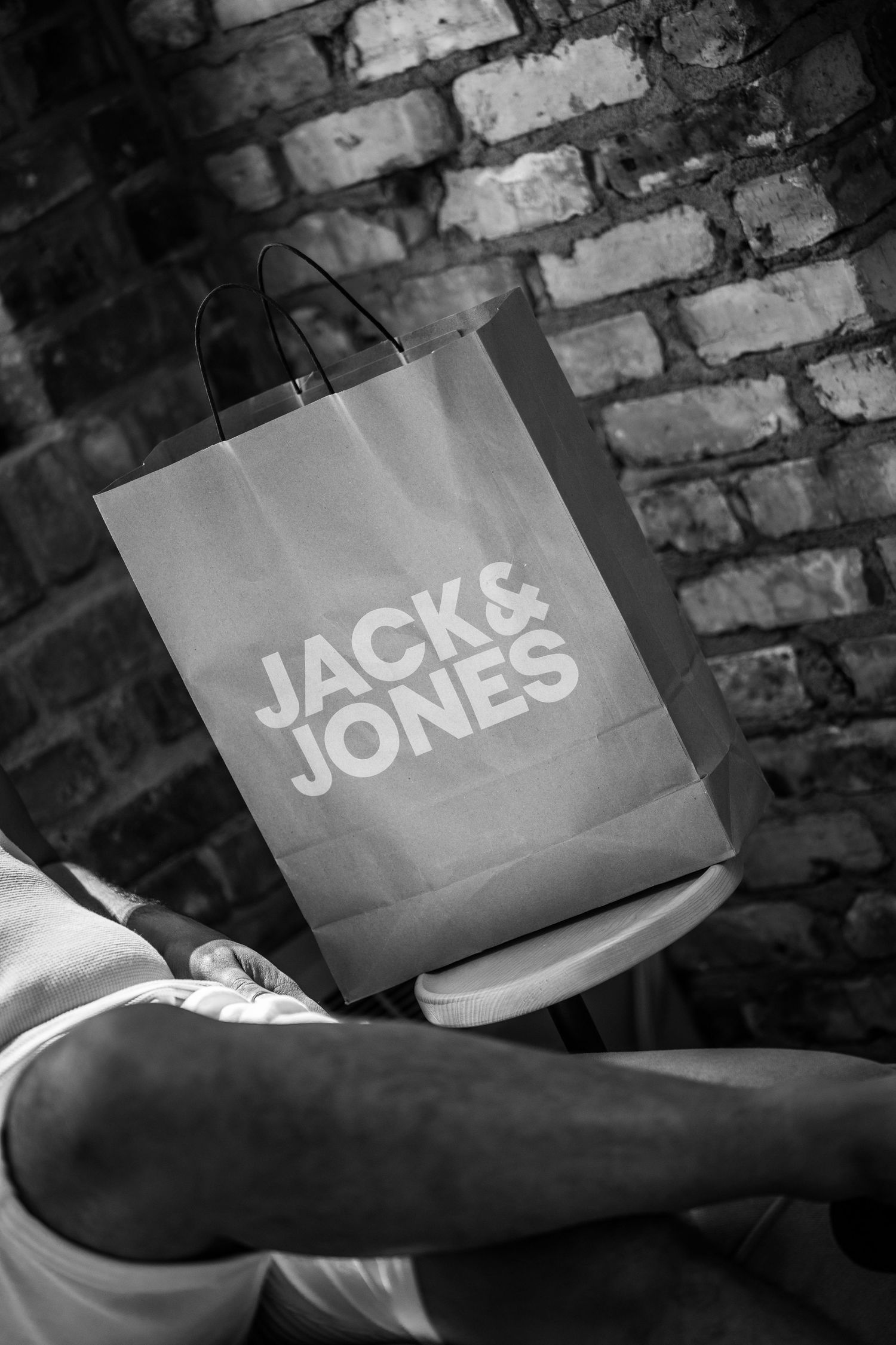 Black and white image of Jack & Jones shopping bags against brick wall.