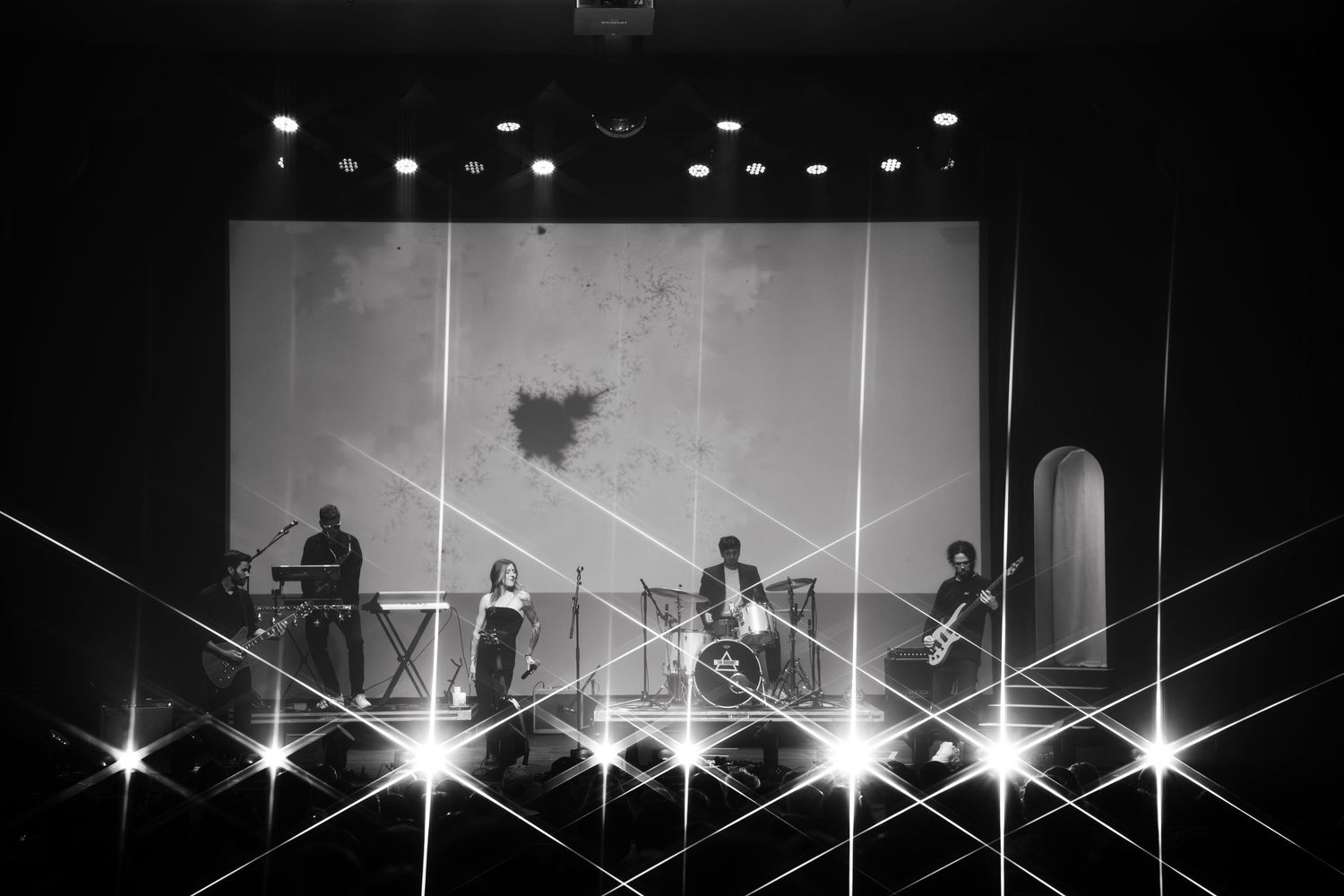 Concert stage illuminated with bright spotlights creating dramatic beams of light in dark venue.