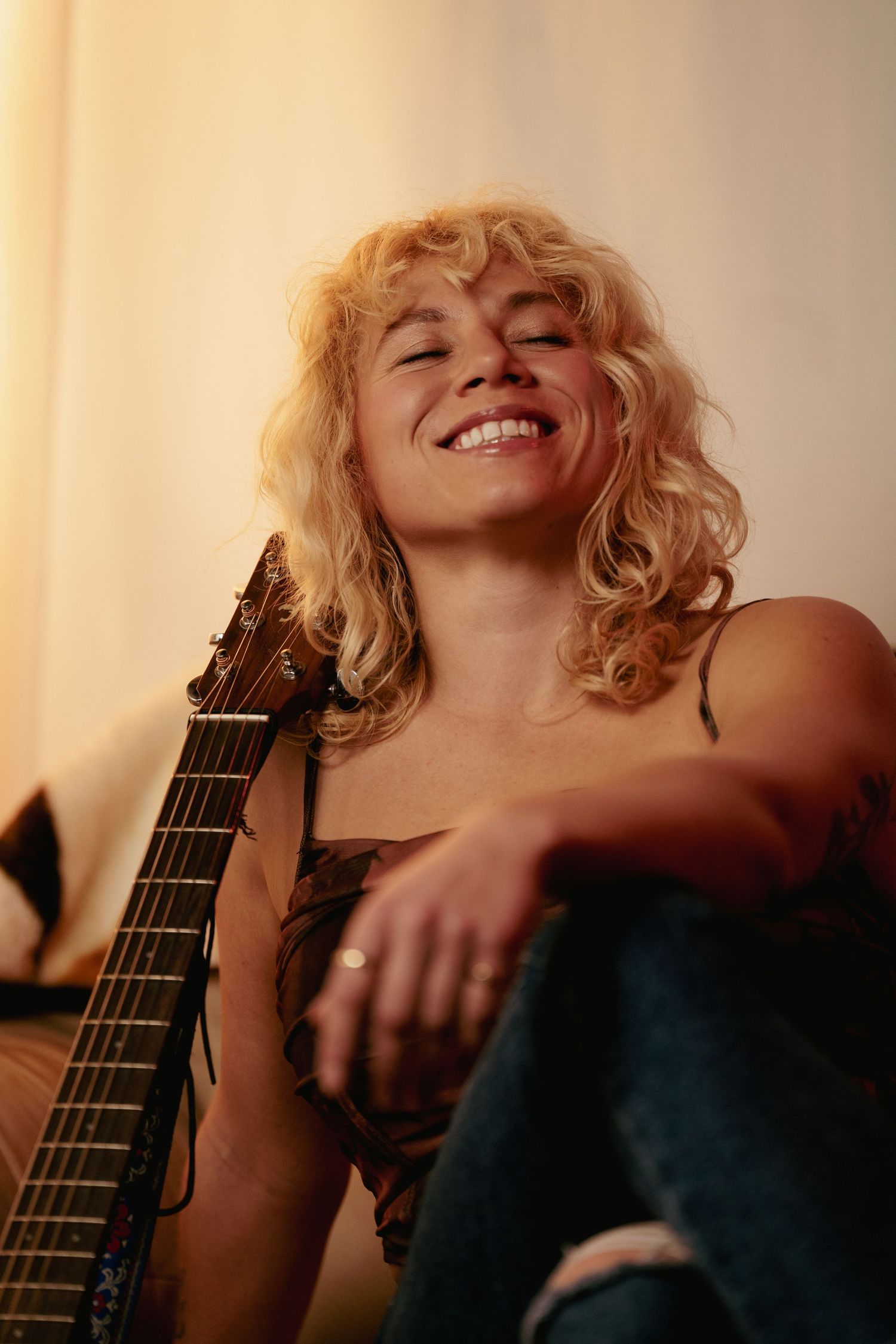 A musician sits with an acoustic guitar in a warmly lit room.