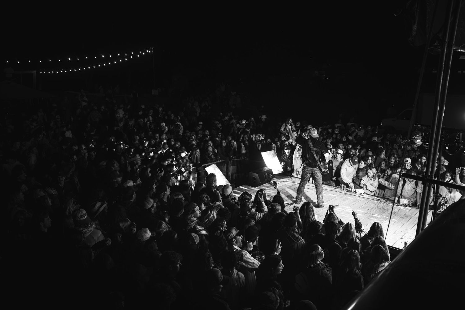 Black and white crowd shot at concert with stage lights illuminating packed audience.