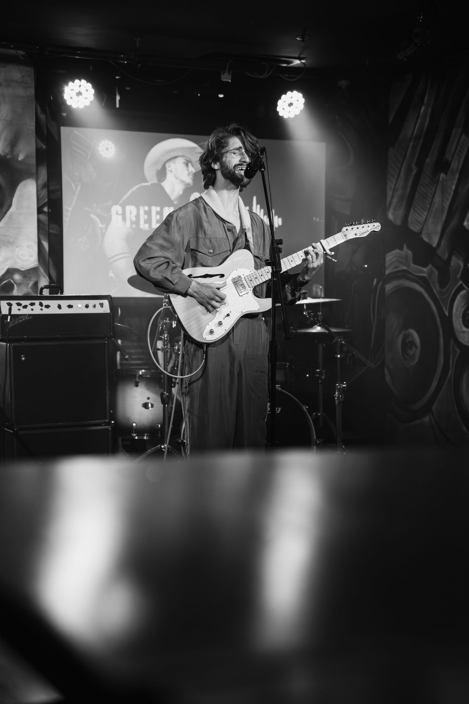 Band performing on a dimly lit stage with projected visuals in the background.