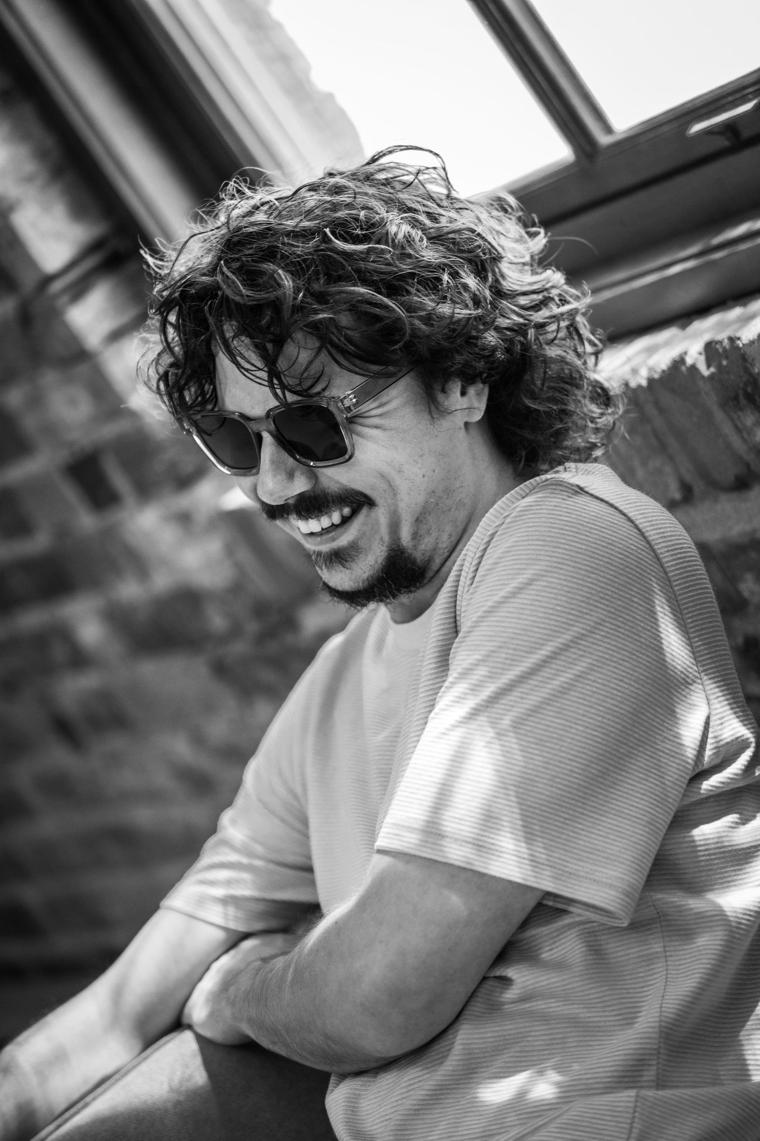 Black and white portrait of someone smiling and wearing sunglasses outdoors.