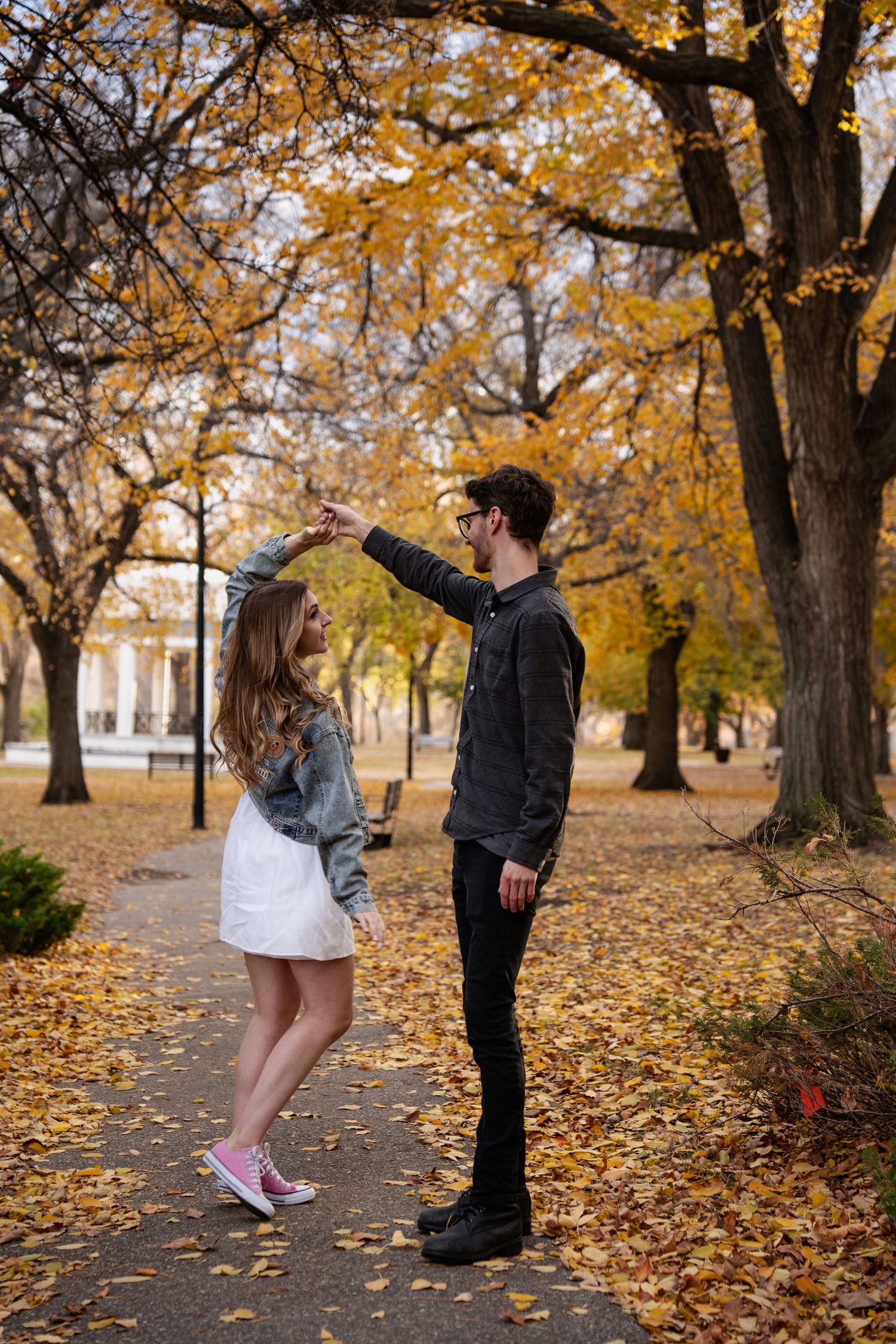 Couple playfully interacting among golden autumn leaves in a park setting.