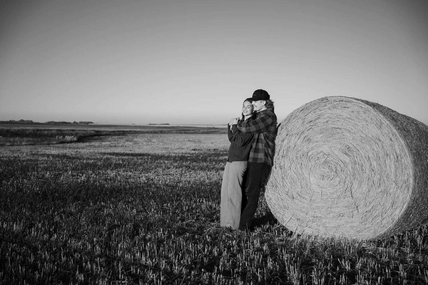 Dramatic black and white landscape with hay bales in a rural field at sunset.