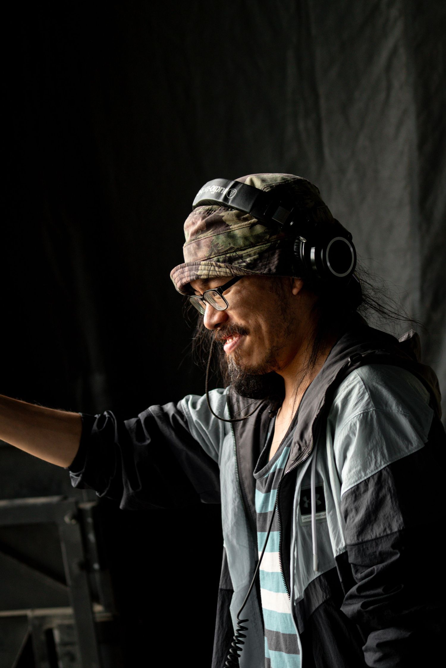 Musician in headphones and cap performs in dramatic side-lit studio setting.