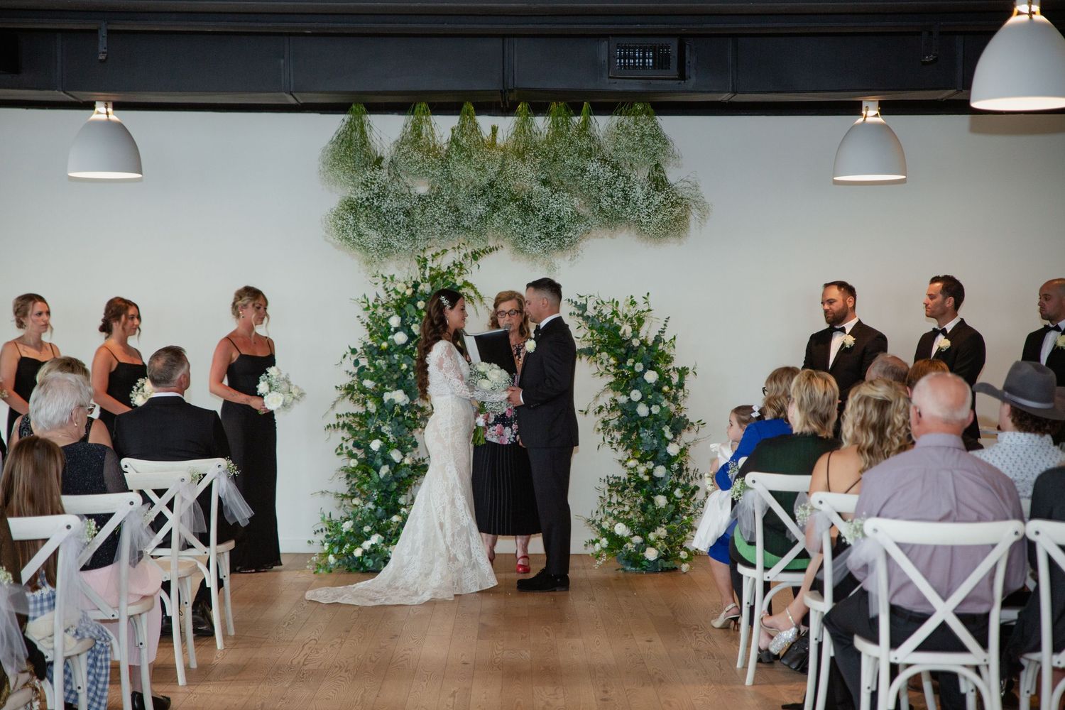 Modern wedding ceremony setup with white chairs and greenery decorations.