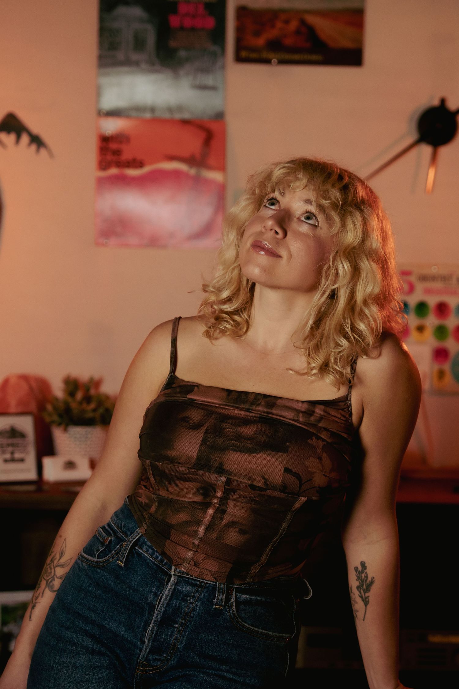 A person in denim and dark top poses casually against a wall with artwork in the background.