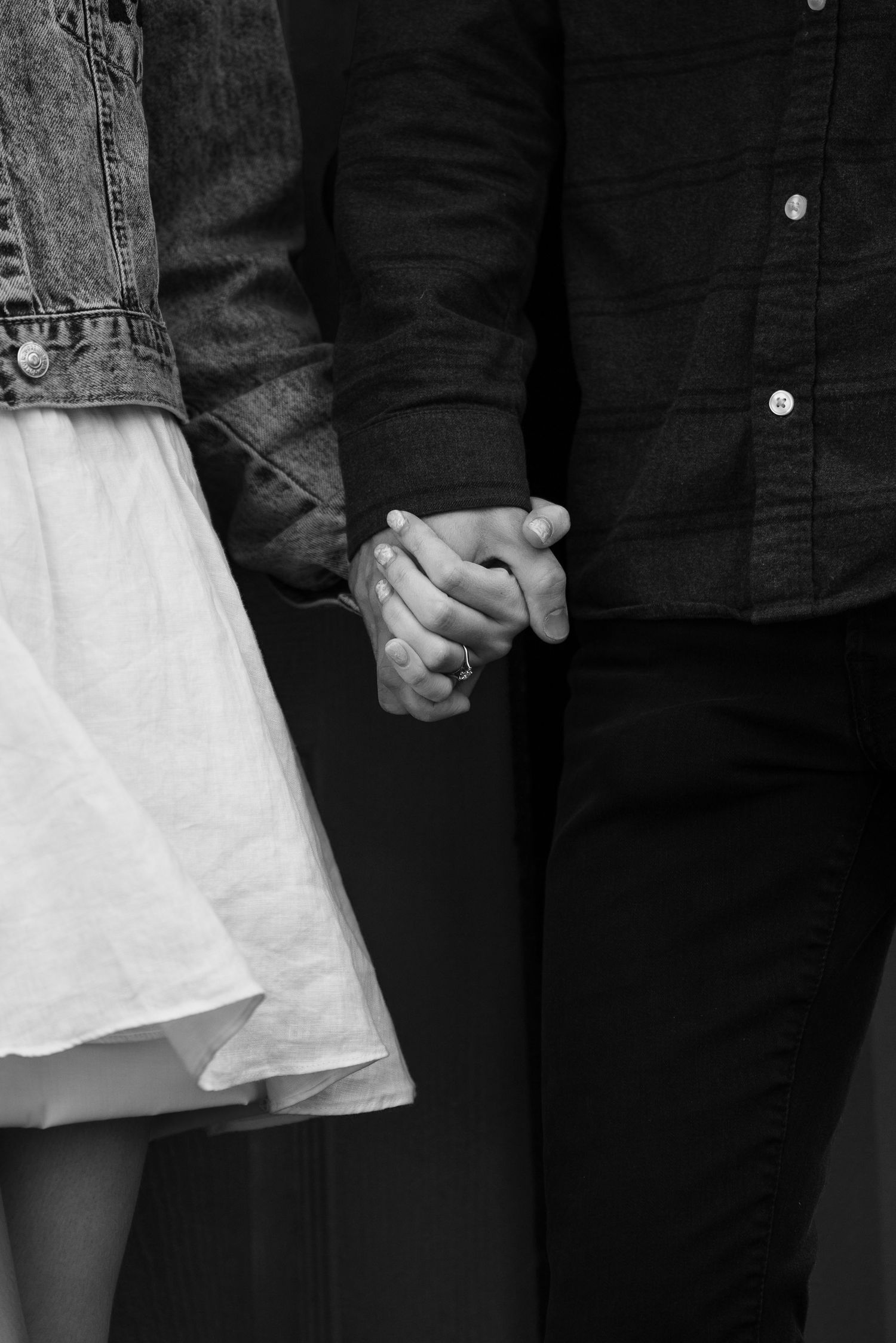 Black and white close-up of couple holding hands, showing denim and white dress details.