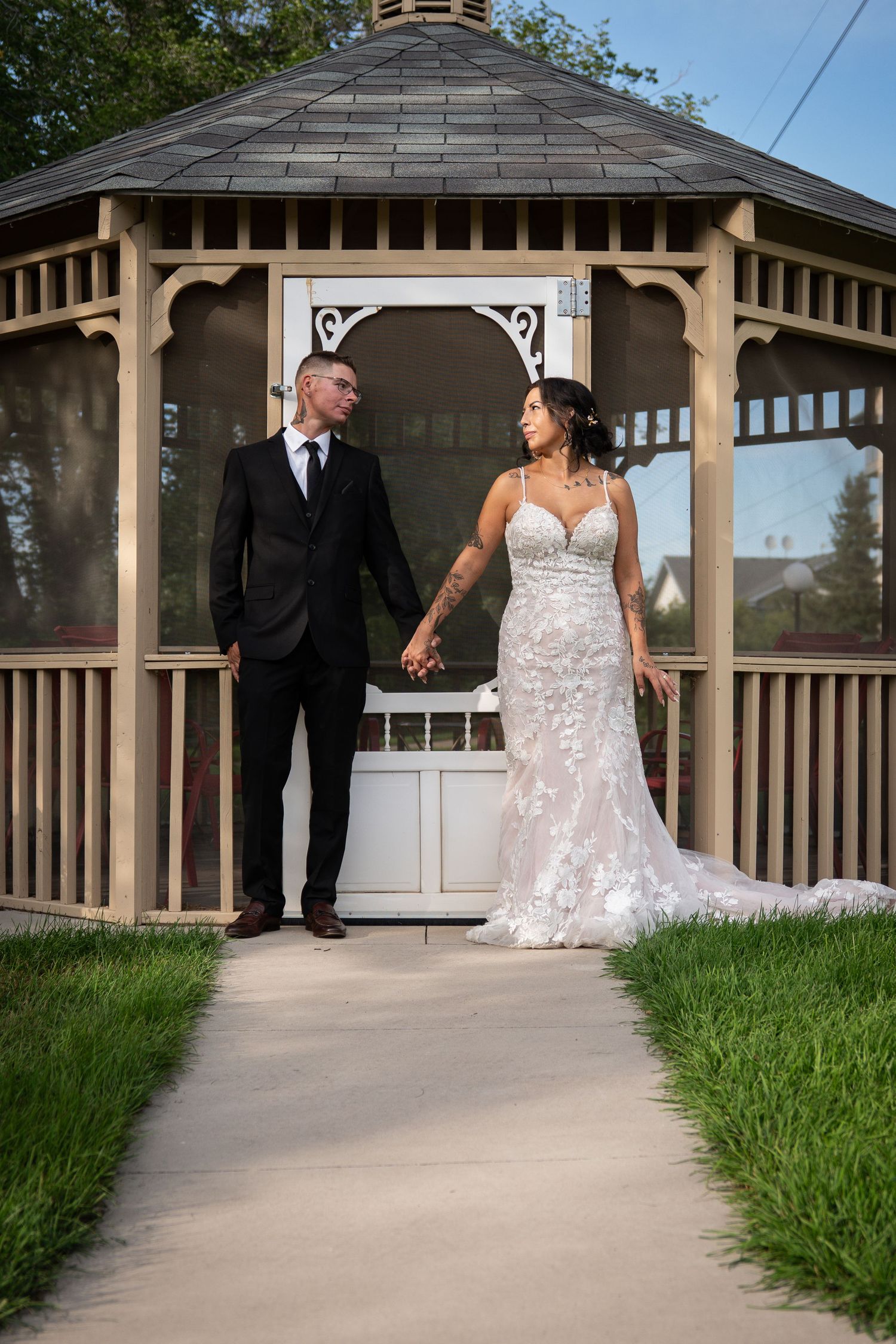 Wedding couple walking along a path near an elegant wooden gazebo.