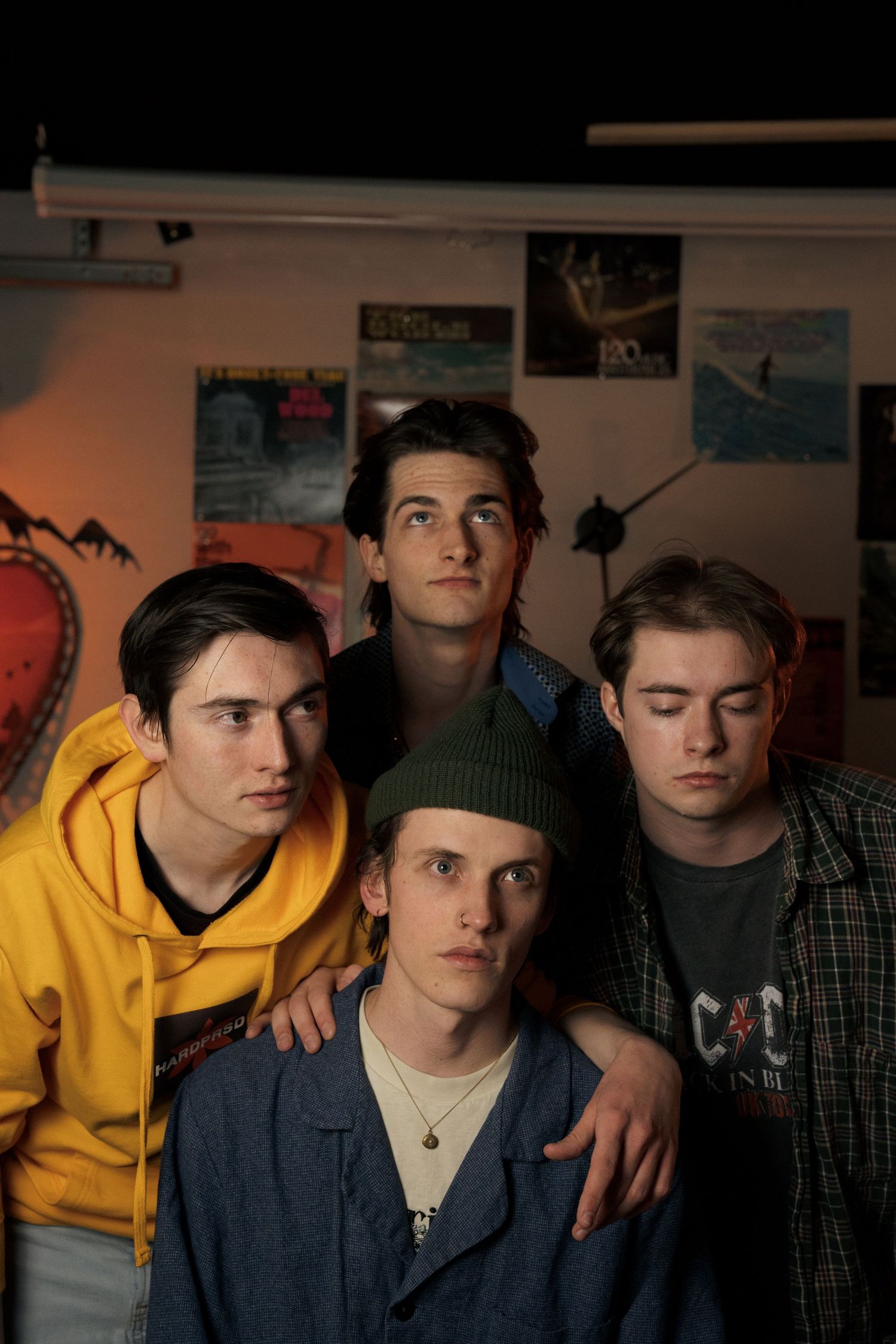 Four young men pose together against wall with posters in moody lighting.