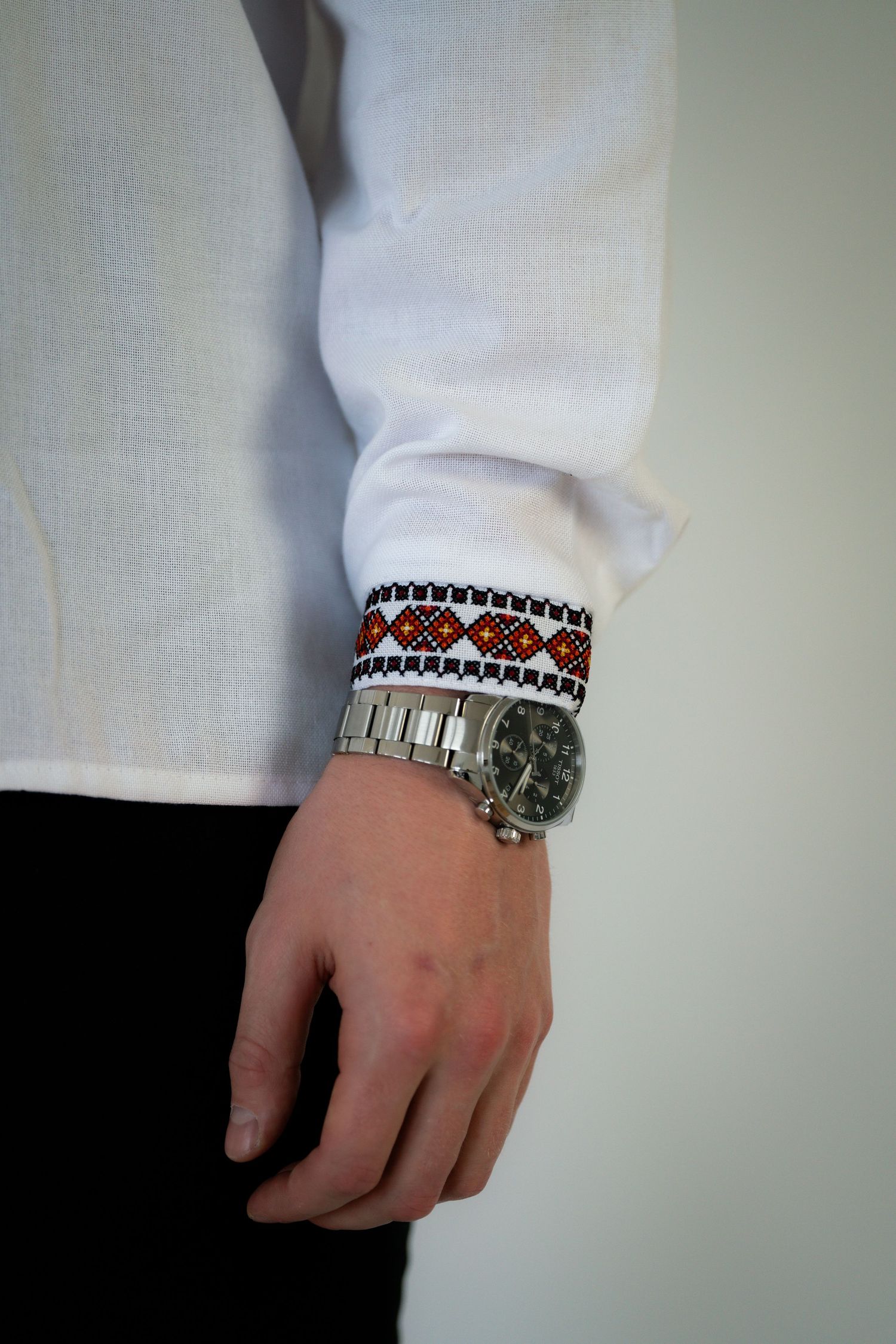 Close-up detail shot of a white sleeve with decorative red and black trim and bracelet.