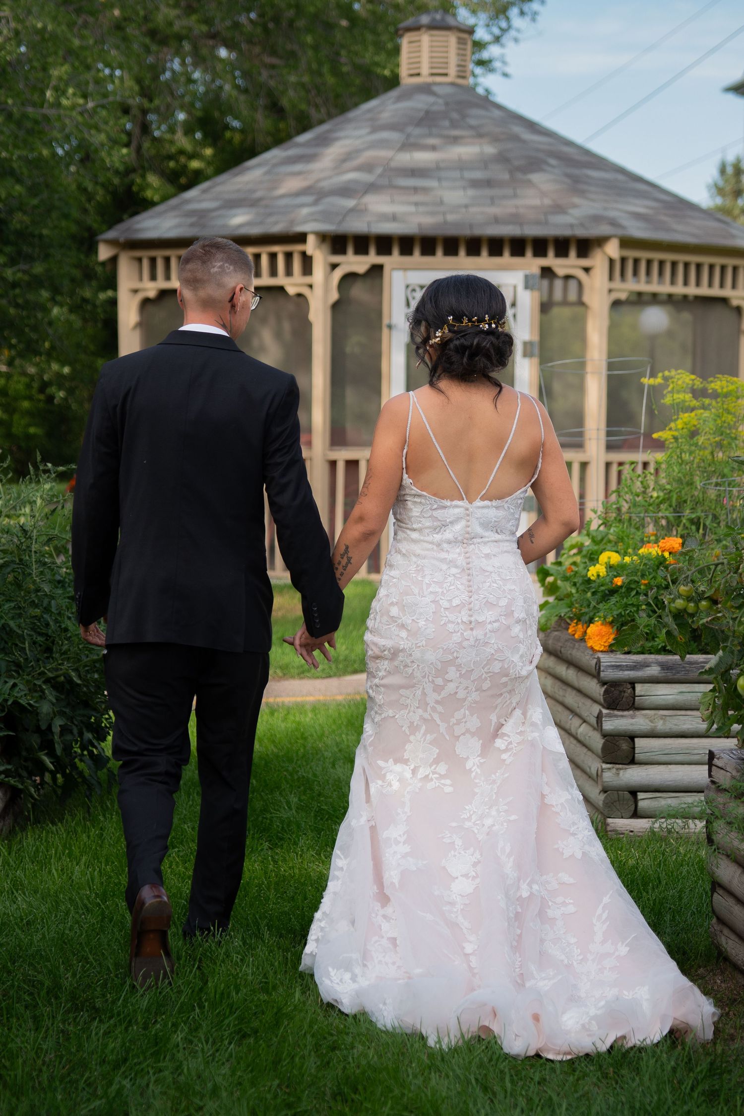 Couple walking through a lush garden path near a wooden gazebo.