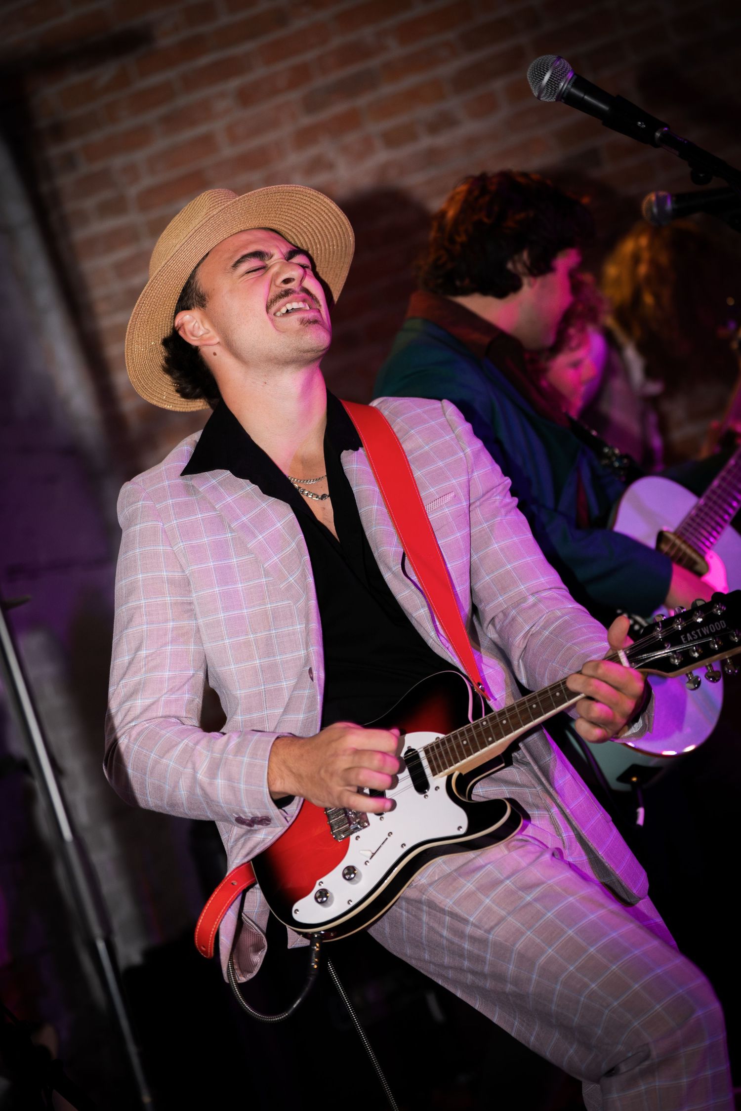 Musician in plaid suit playing banjo with energetic expression during live performance.