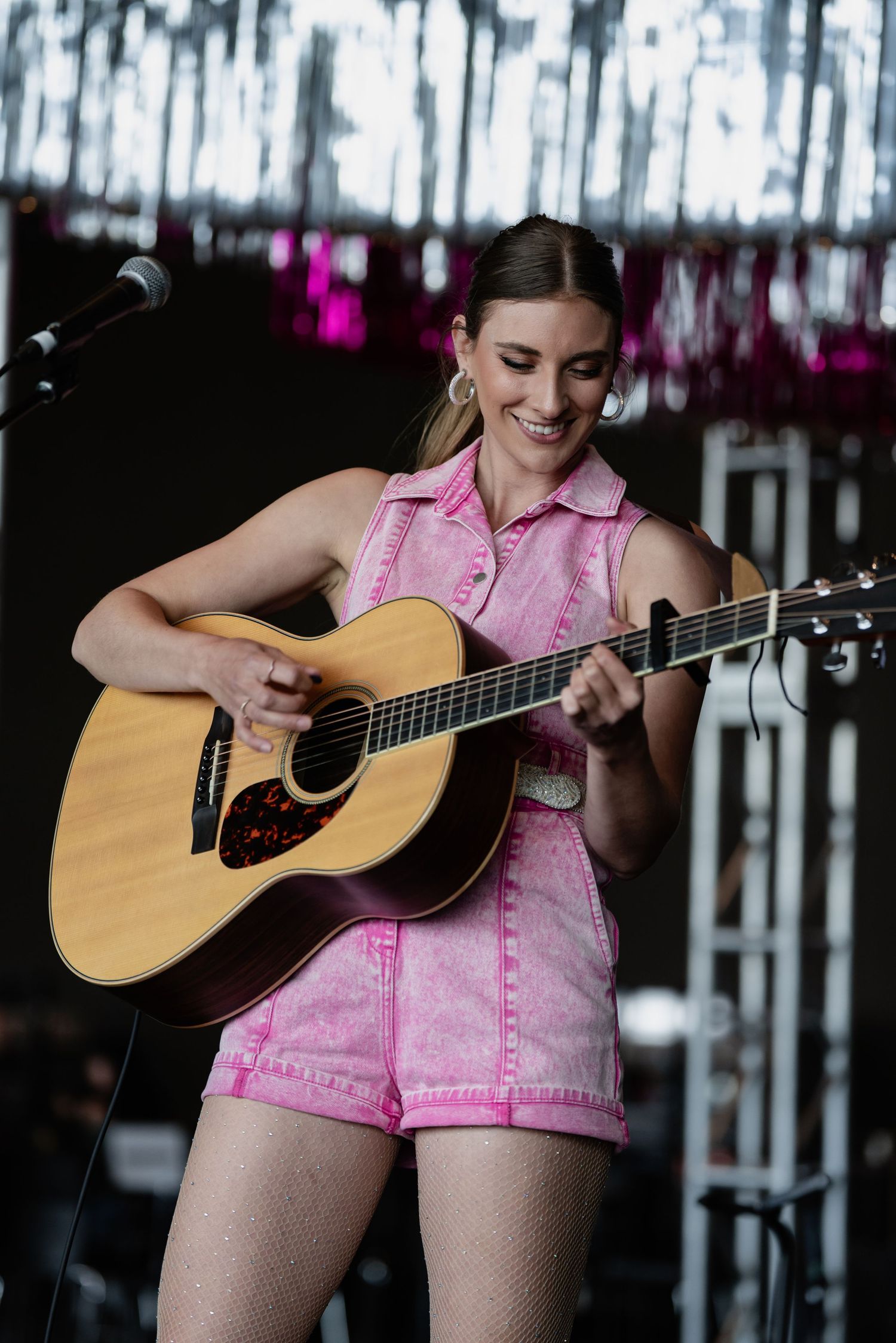 Musician in pink outfit playing acoustic guitar on stage with dynamic movement.