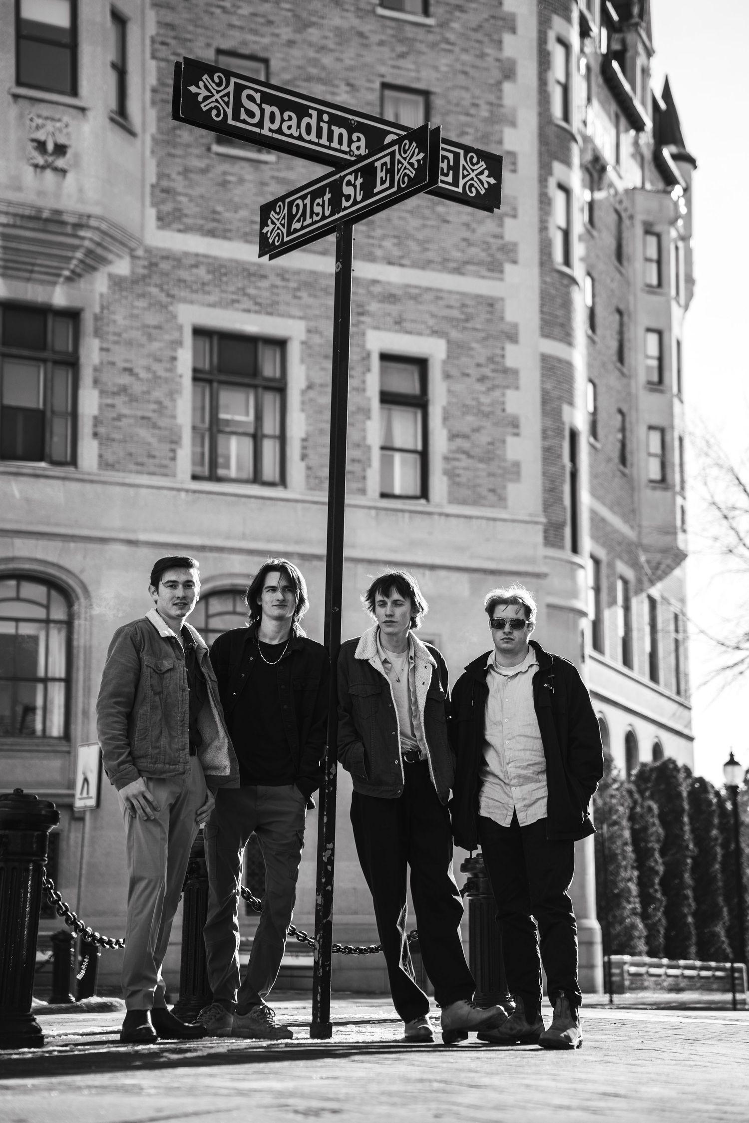 Group standing on urban sidewalk near street sign in black and white photograph.