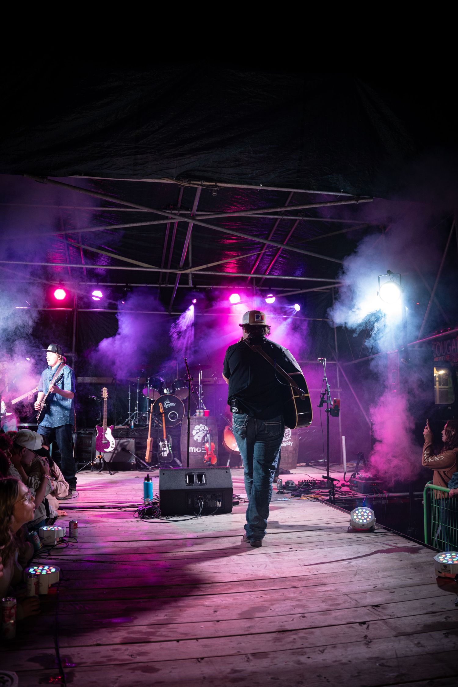 Concert venue with performers silhouetted against purple and pink stage lighting effects.