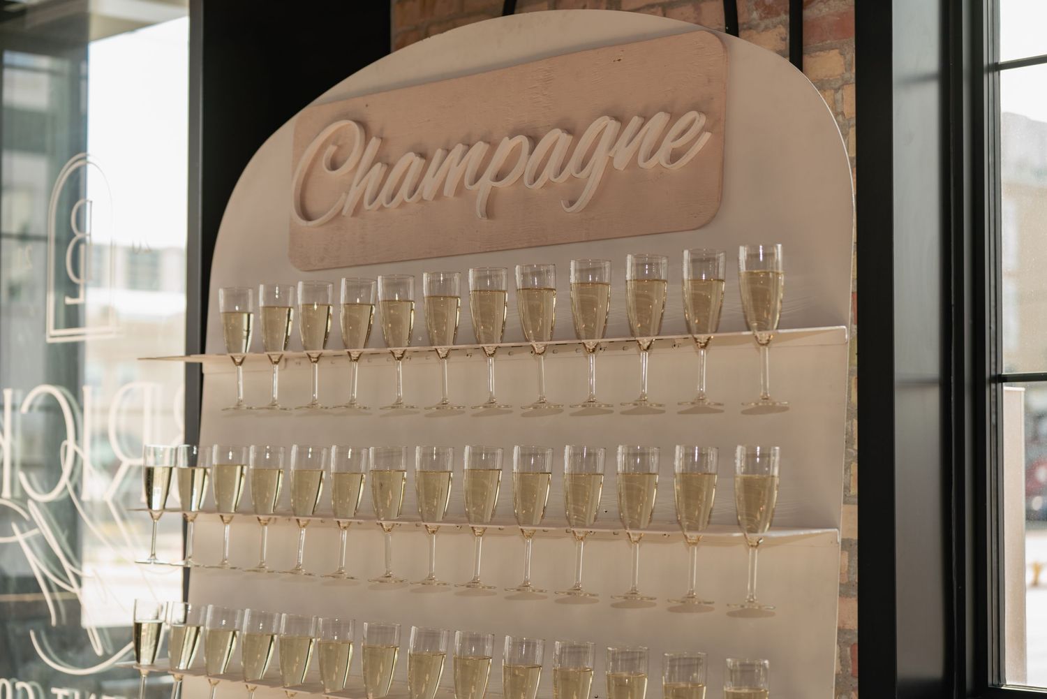 Elegant champagne display wall with rows of empty glasses arranged under cursive signage.