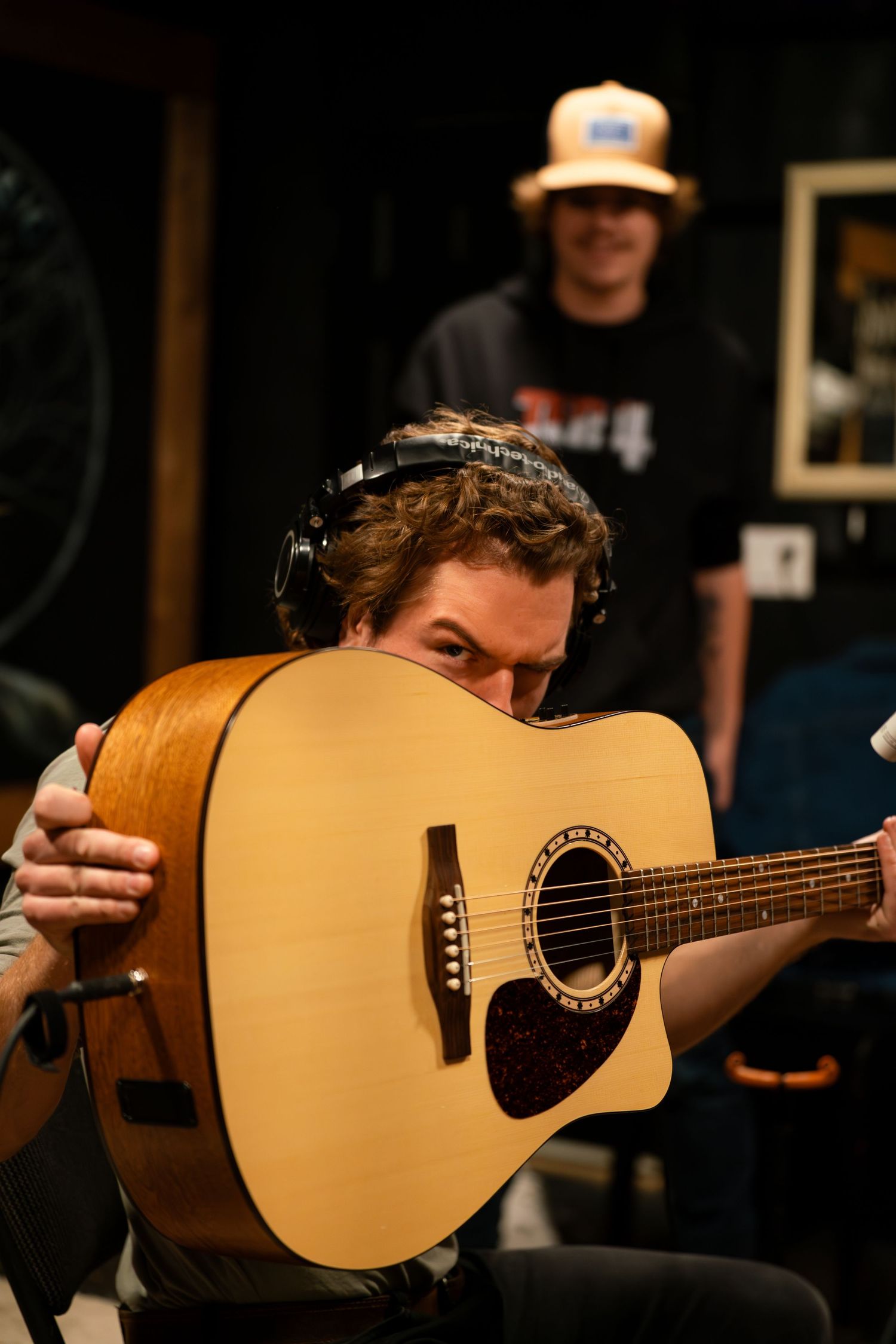 Close-up shot of acoustic guitar being played in recording studio with headphones visible.