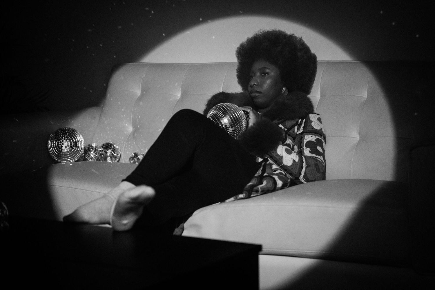 Moody black and white photo of person lounging on couch with disco ball in spotlight.