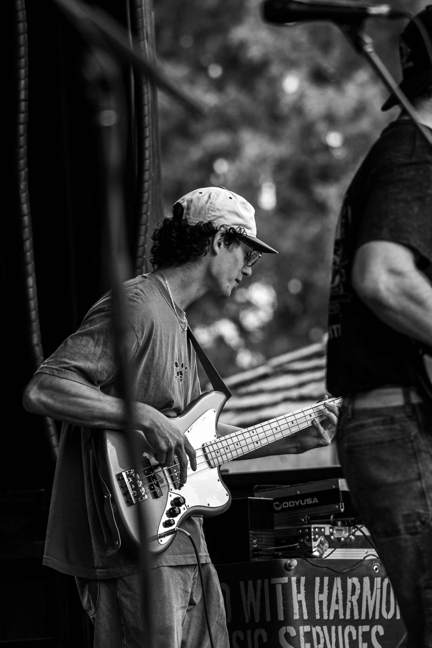 Bass player performing with band equipment and 'Harmony' signage visible in background.