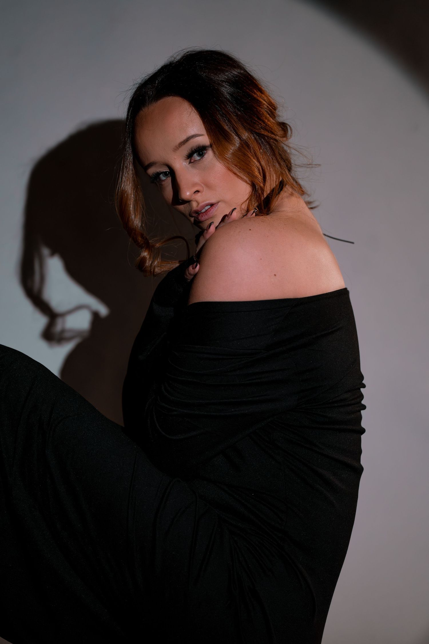 Dramatic portrait of a woman in black off-shoulder dress with moody lighting and shadow effects.