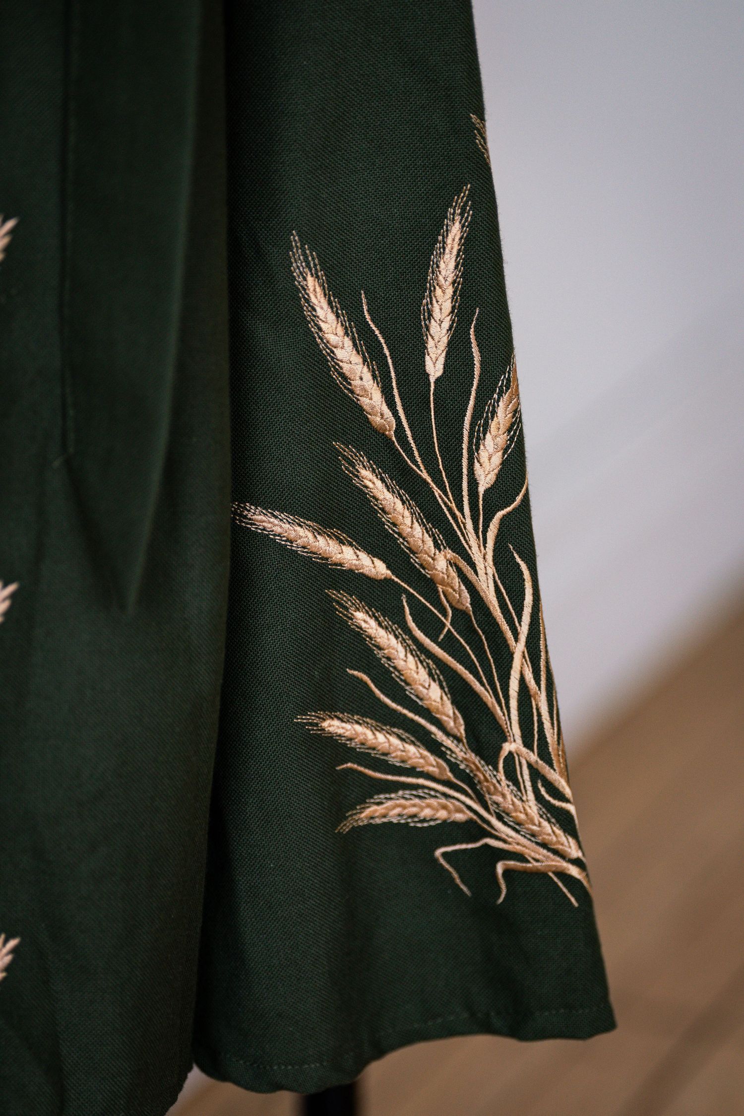 Dark green fabric with golden wheat stalk embroidery pattern detail.