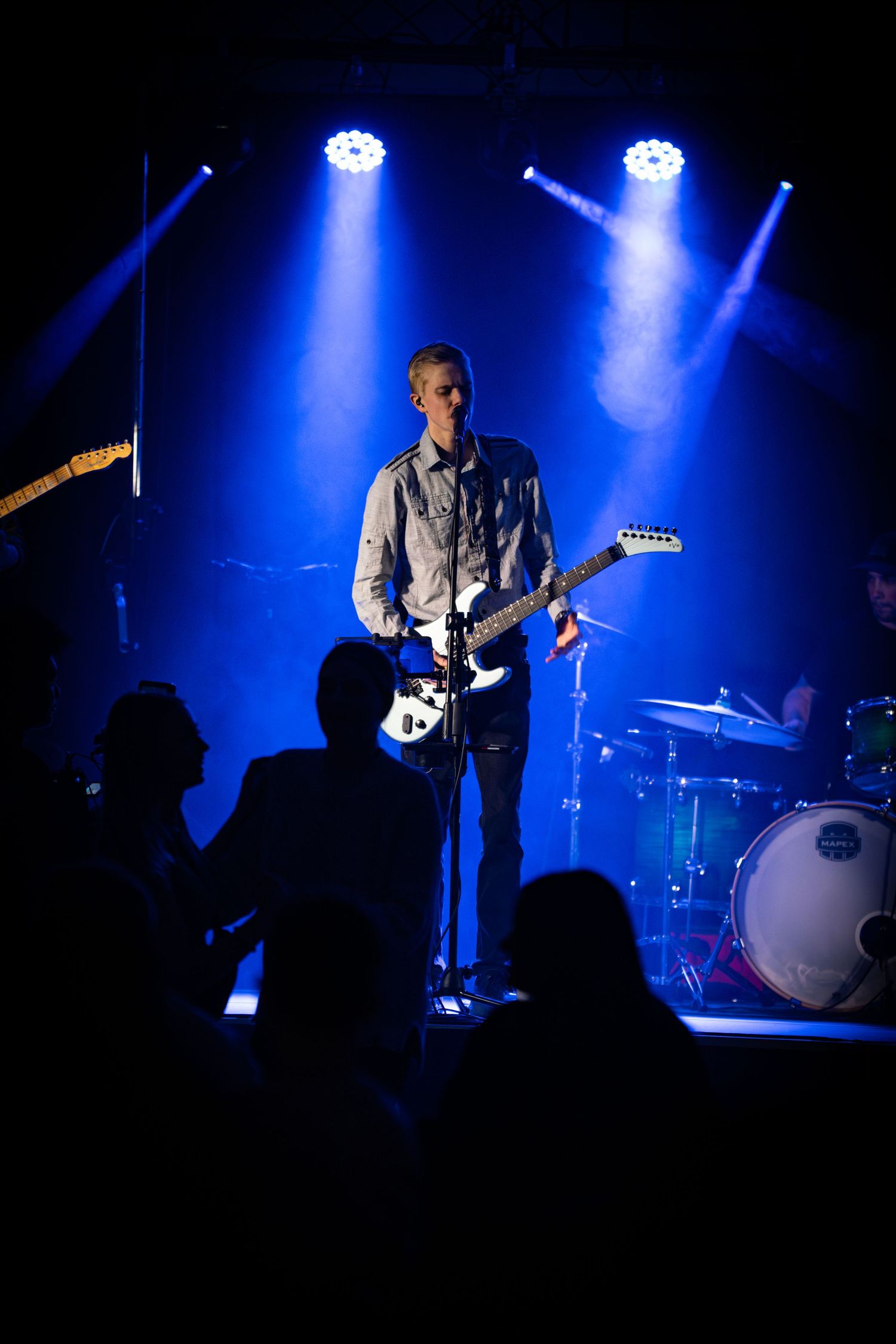 Musician performs under bright blue stage lights with silhouetted crowd visible.