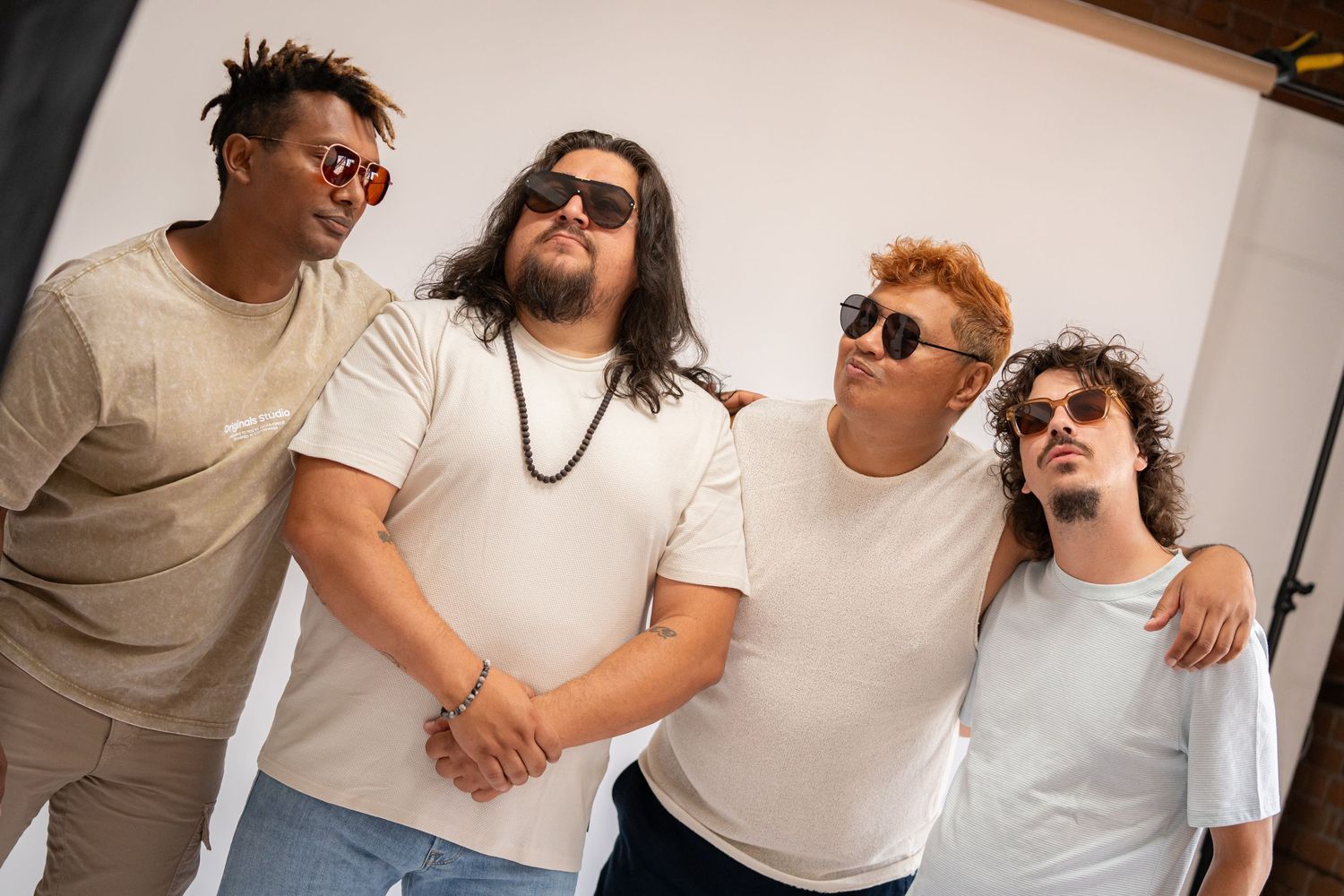 Group photo of four people wearing white shirts and sunglasses posing together against a light background.