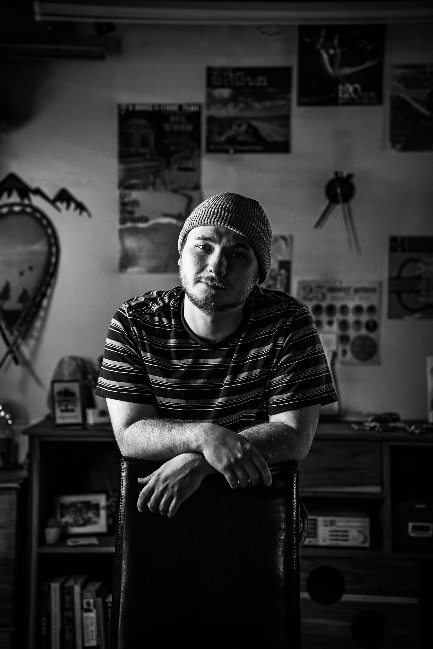 Black and white portrait series of someone wearing a striped shirt and beanie in a room with posters.