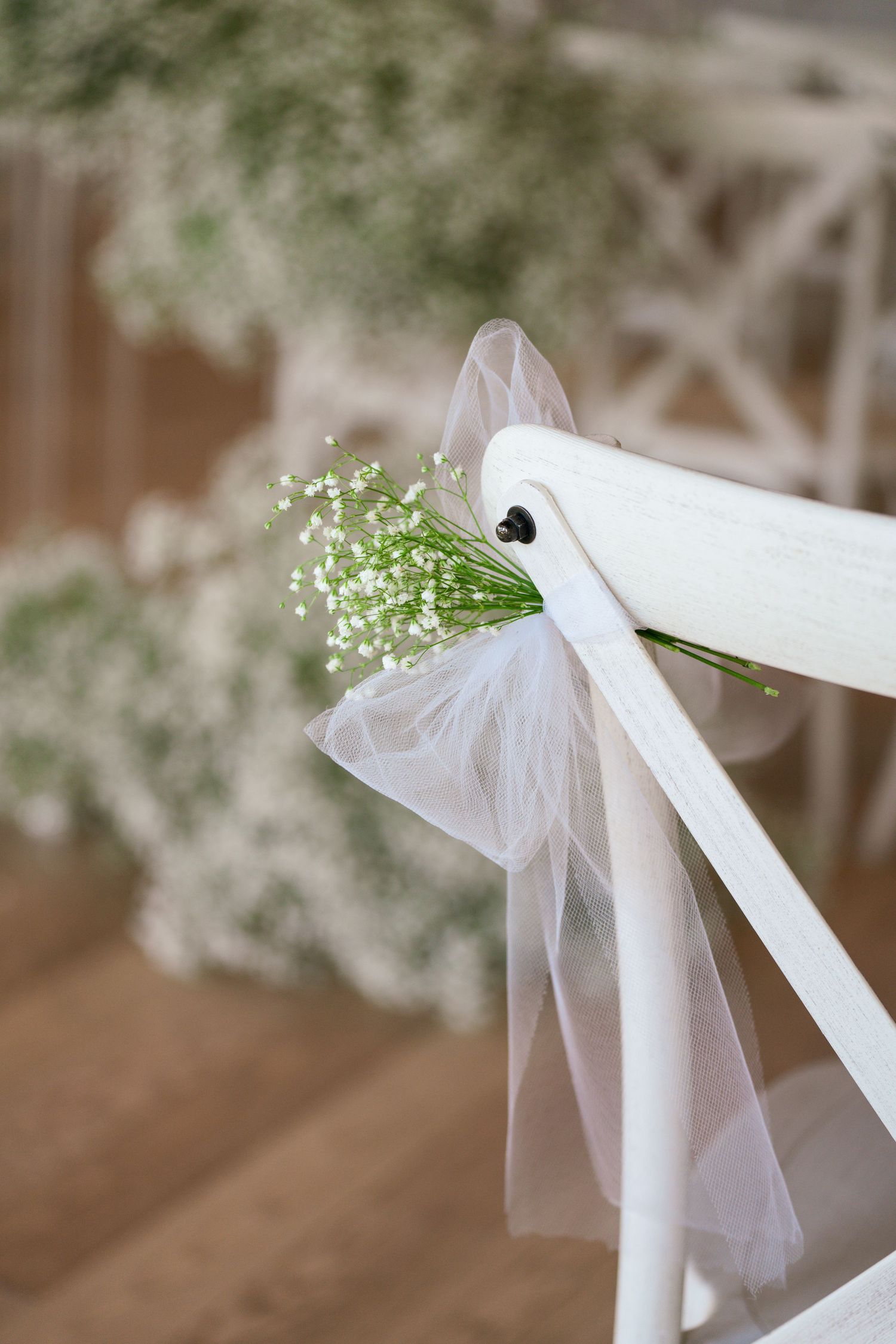 White chair decorated with baby's breath flowers and delicate tulle for a wedding ceremony.