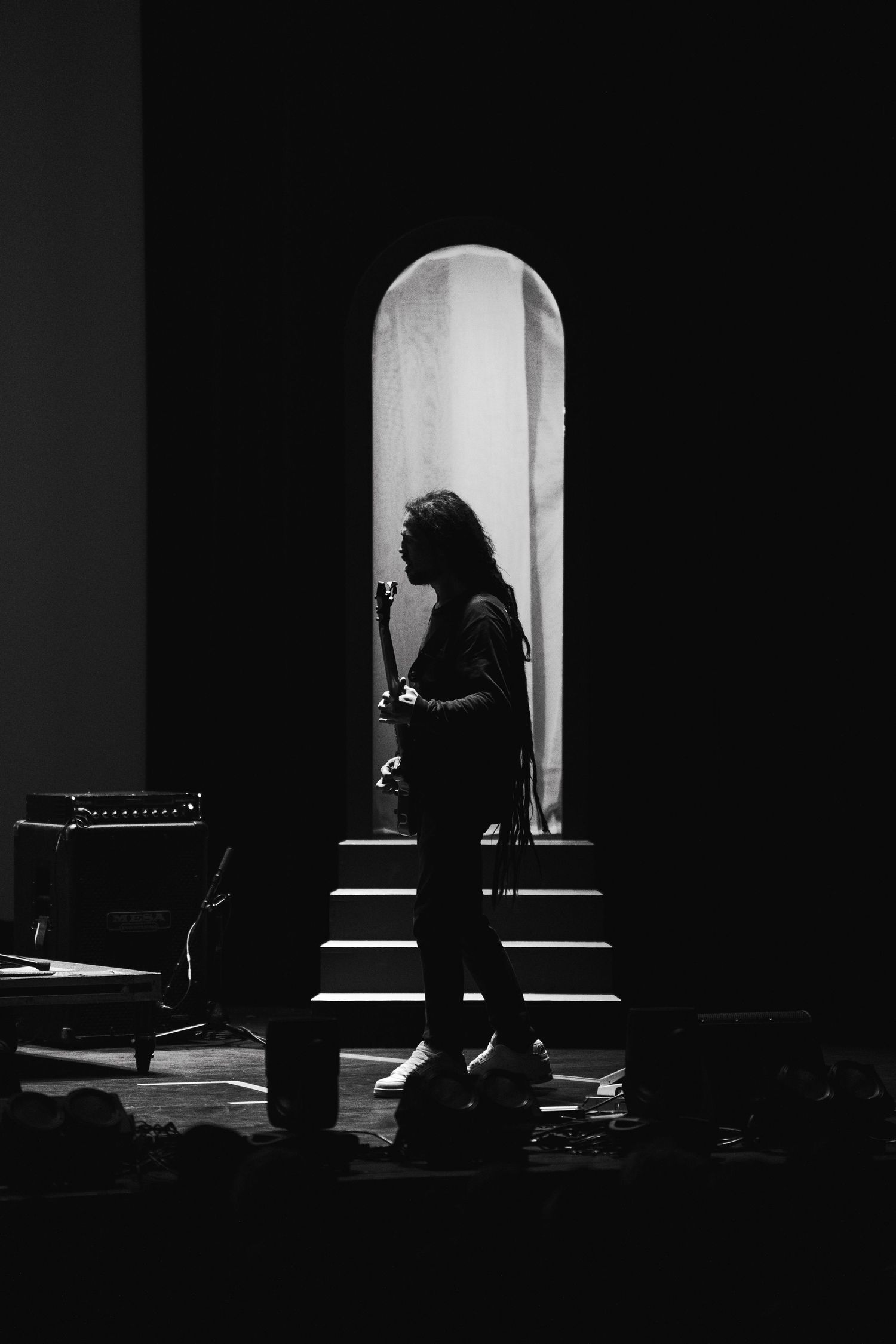 Silhouetted performer stands in dramatic archway lighting during concert performance.