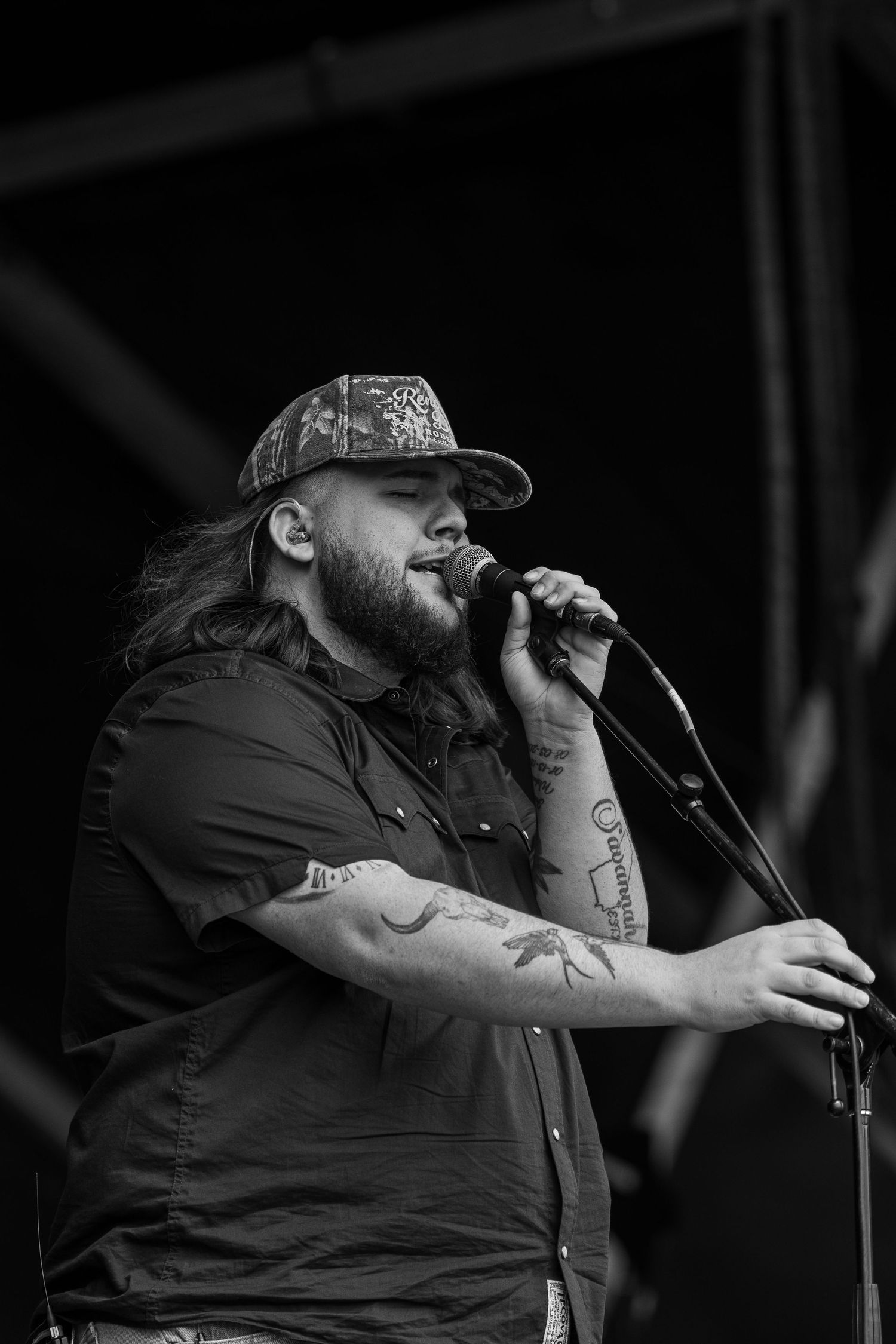 Performer singing into microphone on dark stage in black and white.
