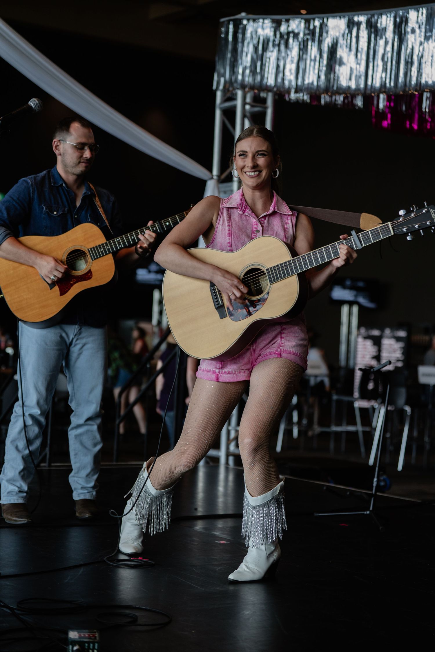 Performer in pink outfit and white boots playing guitar during energetic stage performance.